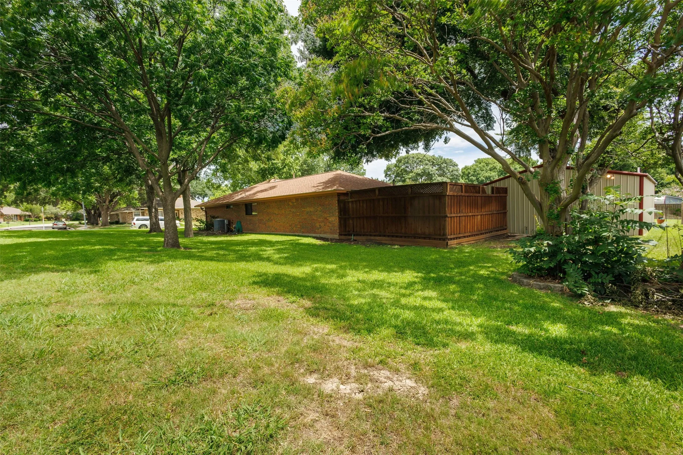 Expansive grassy yard featuring mature trees, a privacy fence, and a storage shed