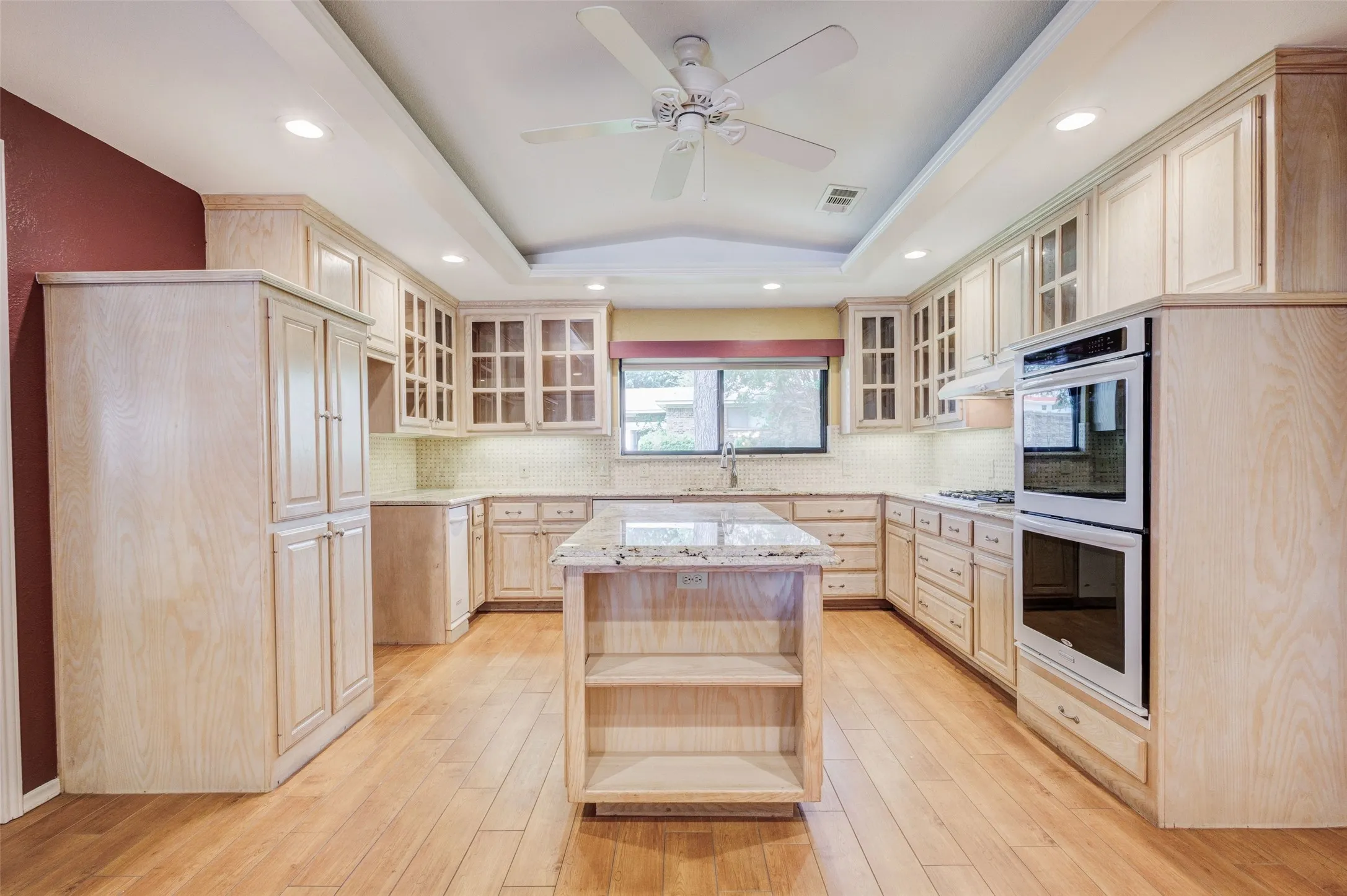 Spacious kitchen featuring wood-finish flooring, extensive light-toned cabinetry, a central island with countertop, double wall ovens, and recessed lighting