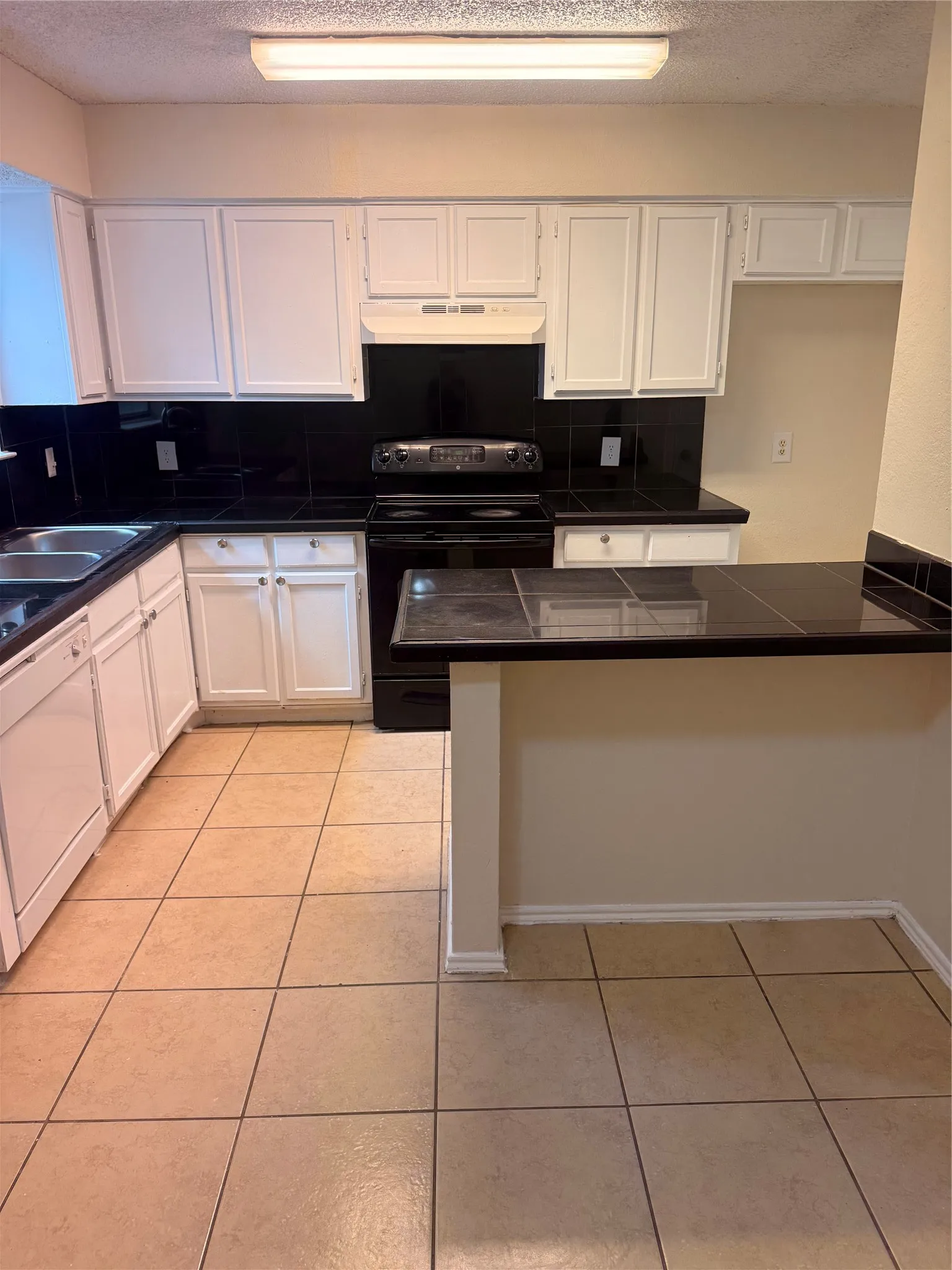Kitchen featuring white cabinetry, black tile backsplash, black countertops, and a built-in breakfast bar