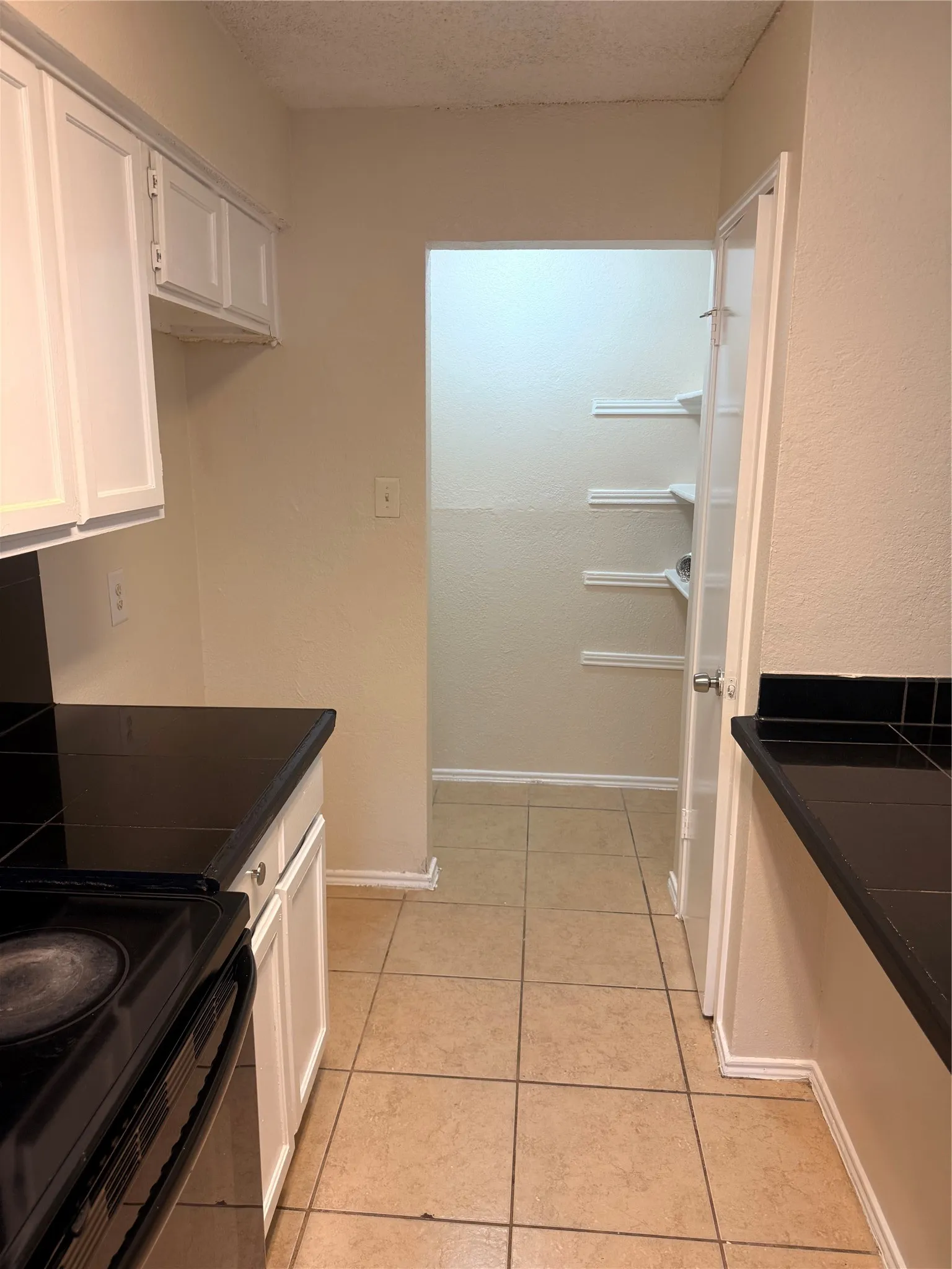 Kitchen featuring a built-in pantry with shelving, tile flooring, white cabinetry, black countertops, and a built-in range