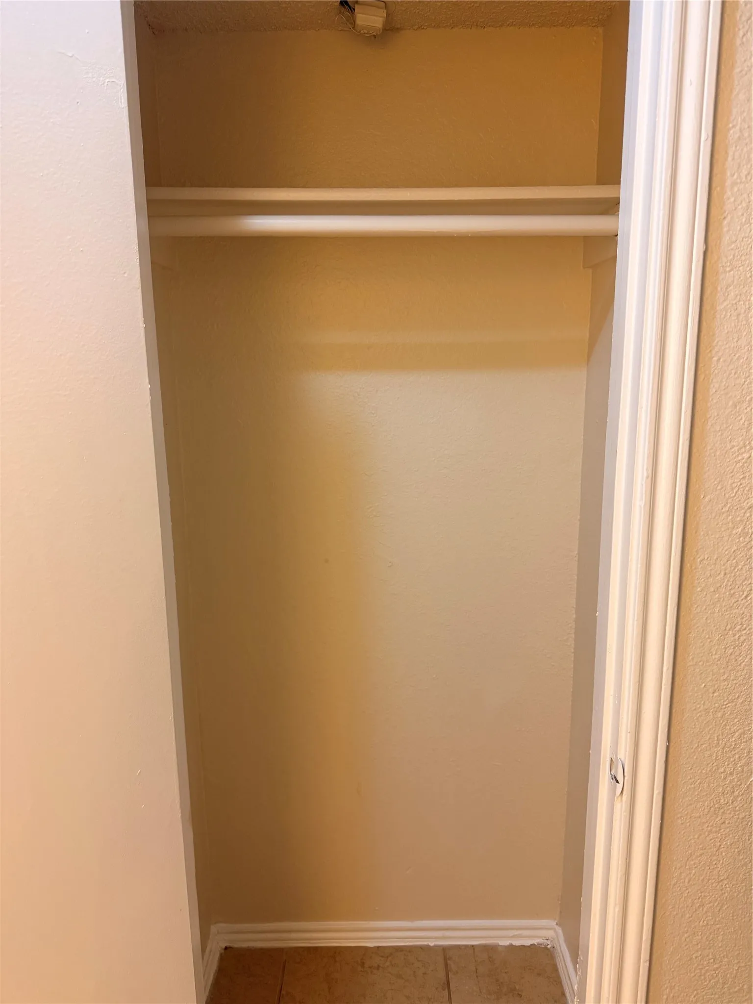 Interior closet space featuring dual clothes rods, an upper shelf, textured walls, and tile flooring