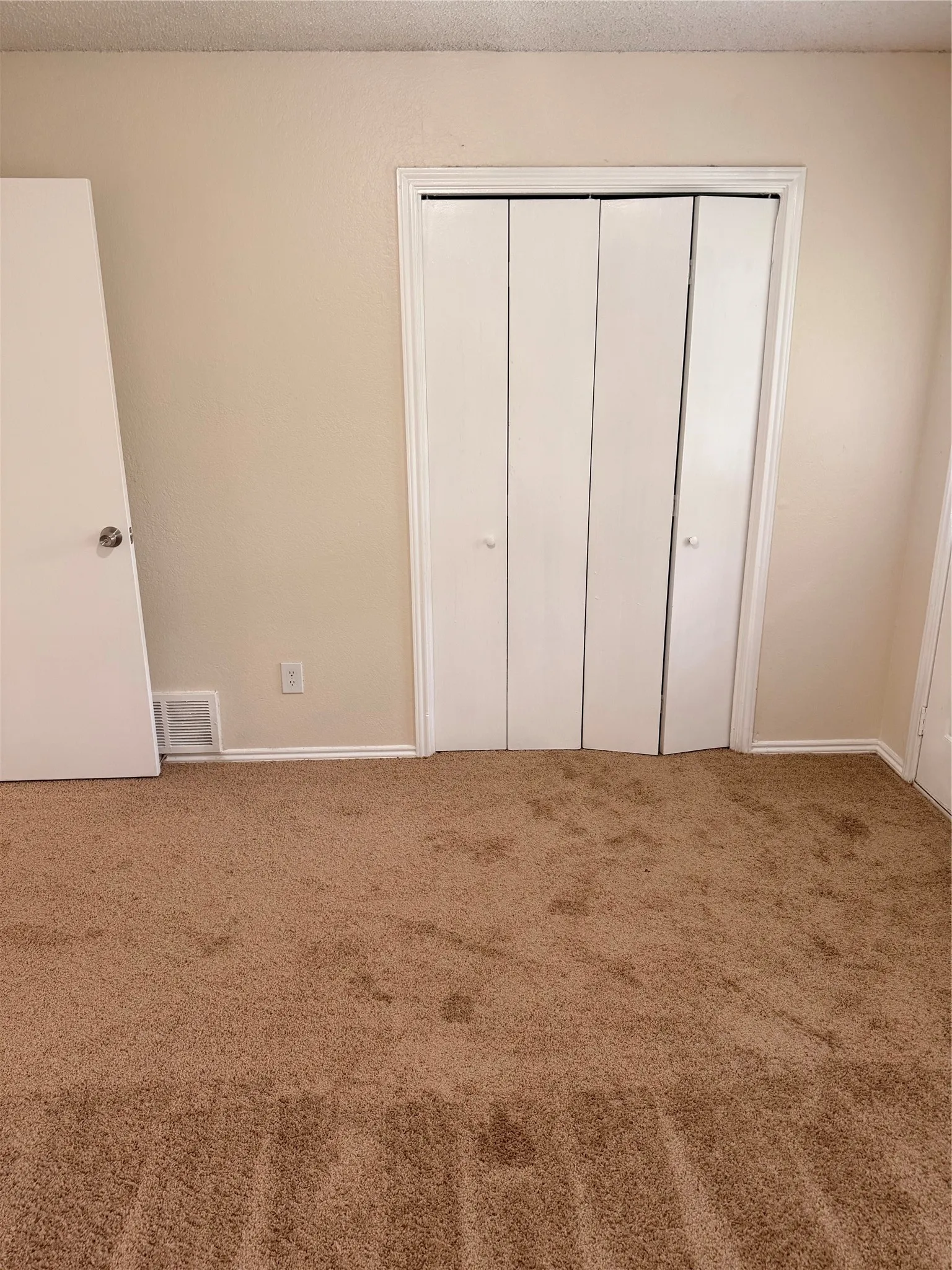 Bedroom featuring neutral tone walls, beige carpet flooring, and a white bi-fold closet