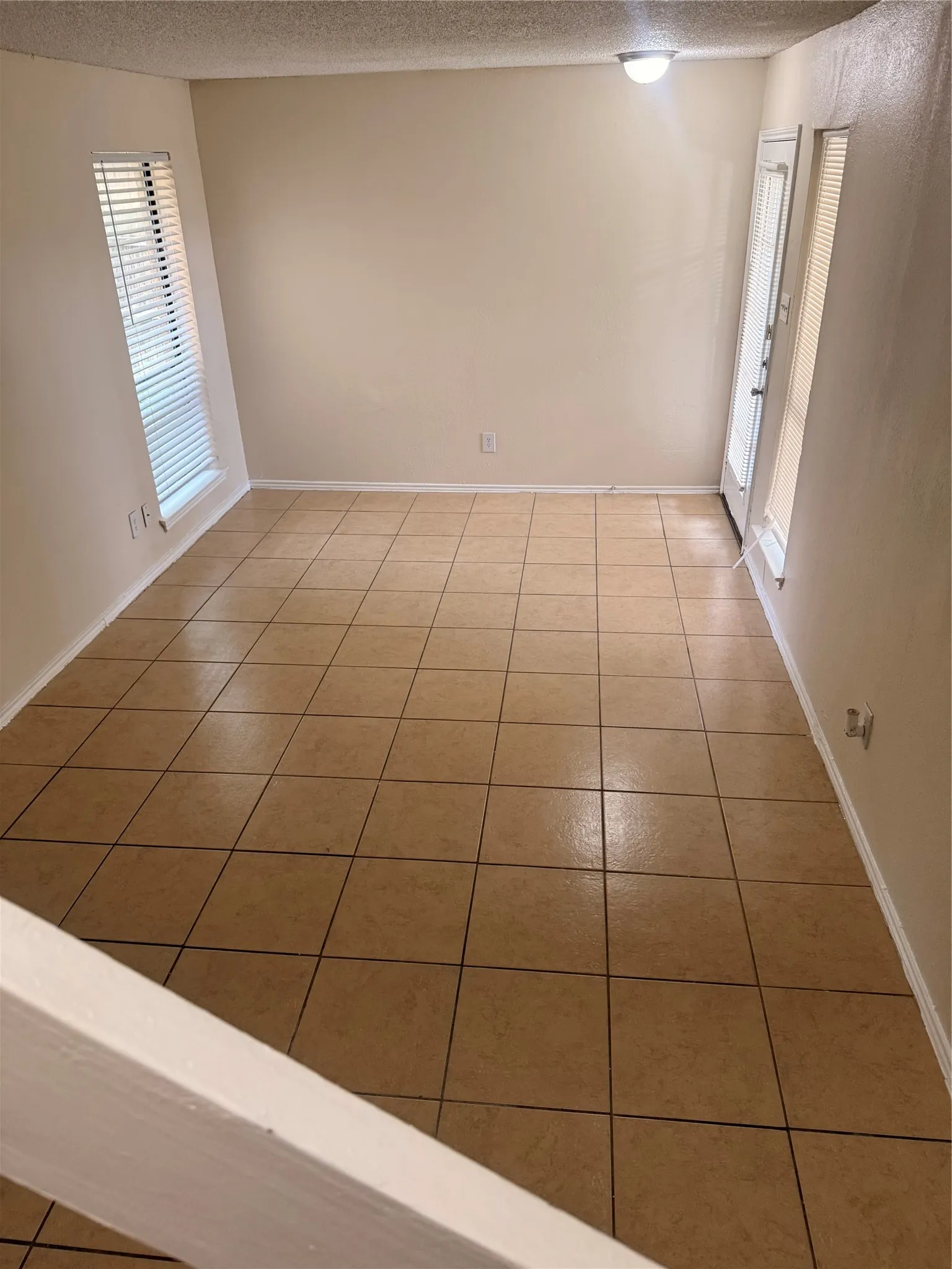 Spacious room featuring neutral-toned tile flooring, light-colored walls, and a ceiling-mounted light fixture