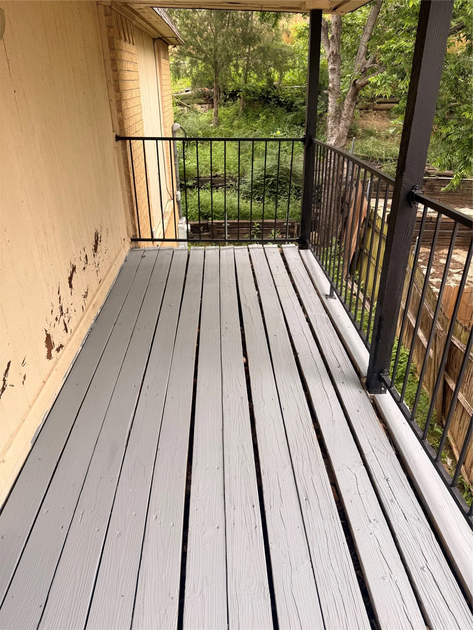 Outdoor deck featuring painted wood-finish planks, black metal railings, and a partial wood-paneled exterior