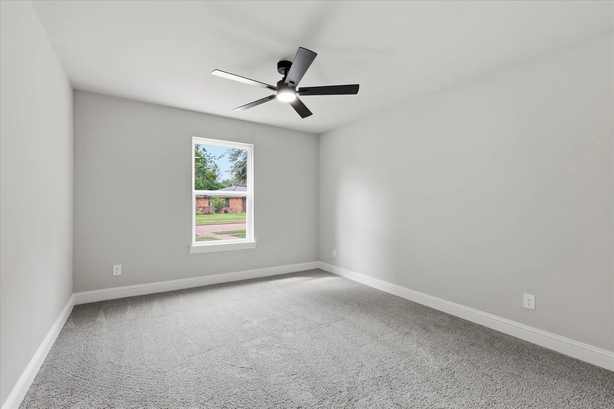 Light gray wall paint, gray carpet flooring, white trim, single window, and a ceiling fan