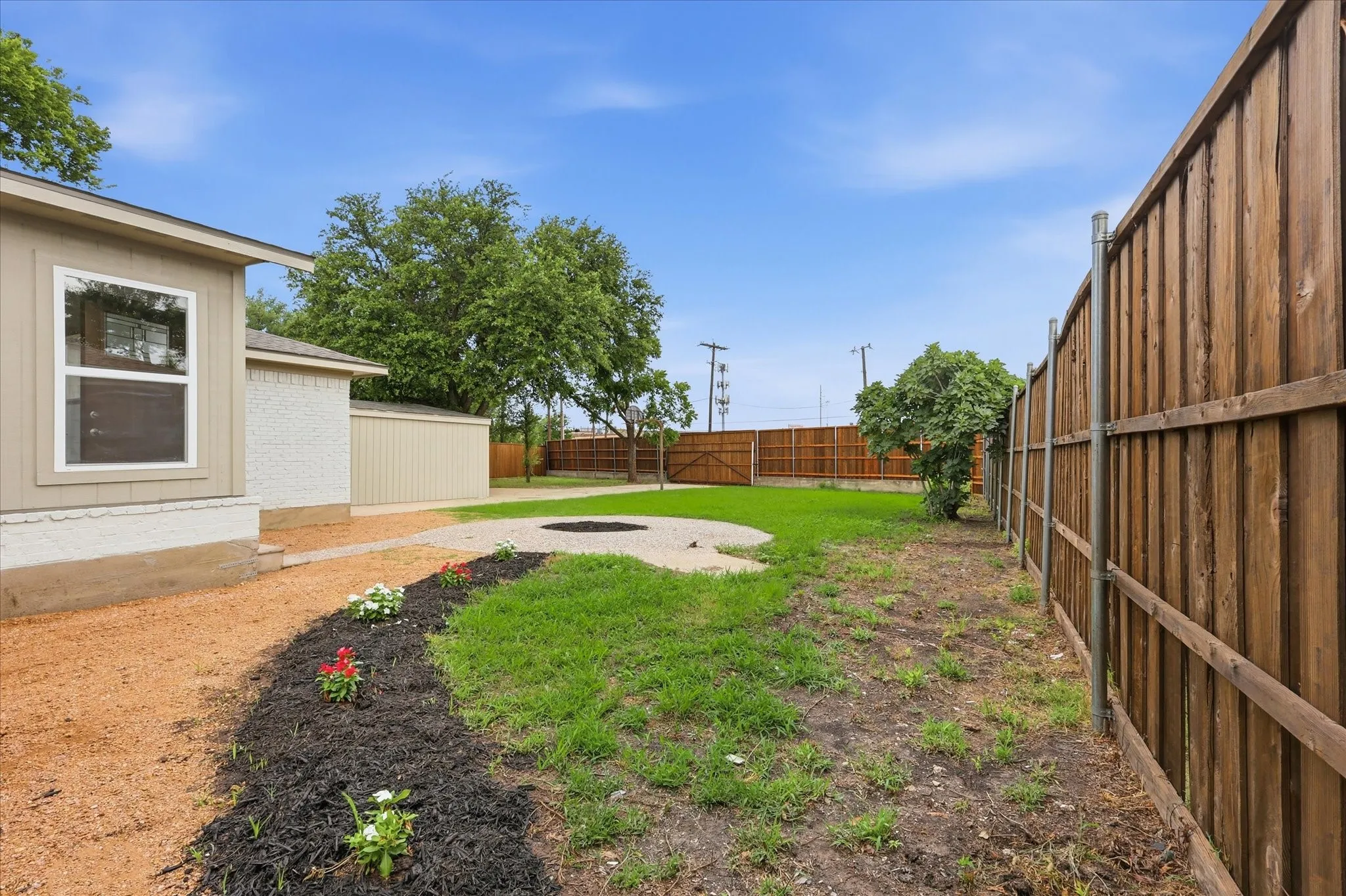 Expansive backyard featuring a circular fire pit area, a landscaped gravel path, and a wood privacy fence