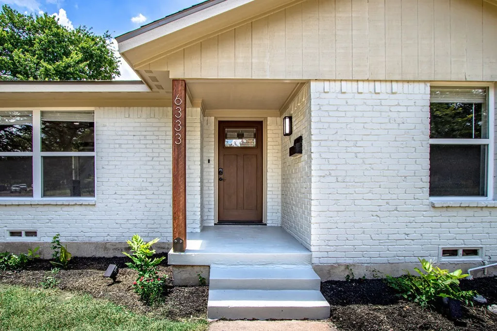 Exterior featuring white-painted brick, a wooden entry door with an upper glass panel, and a covered porch