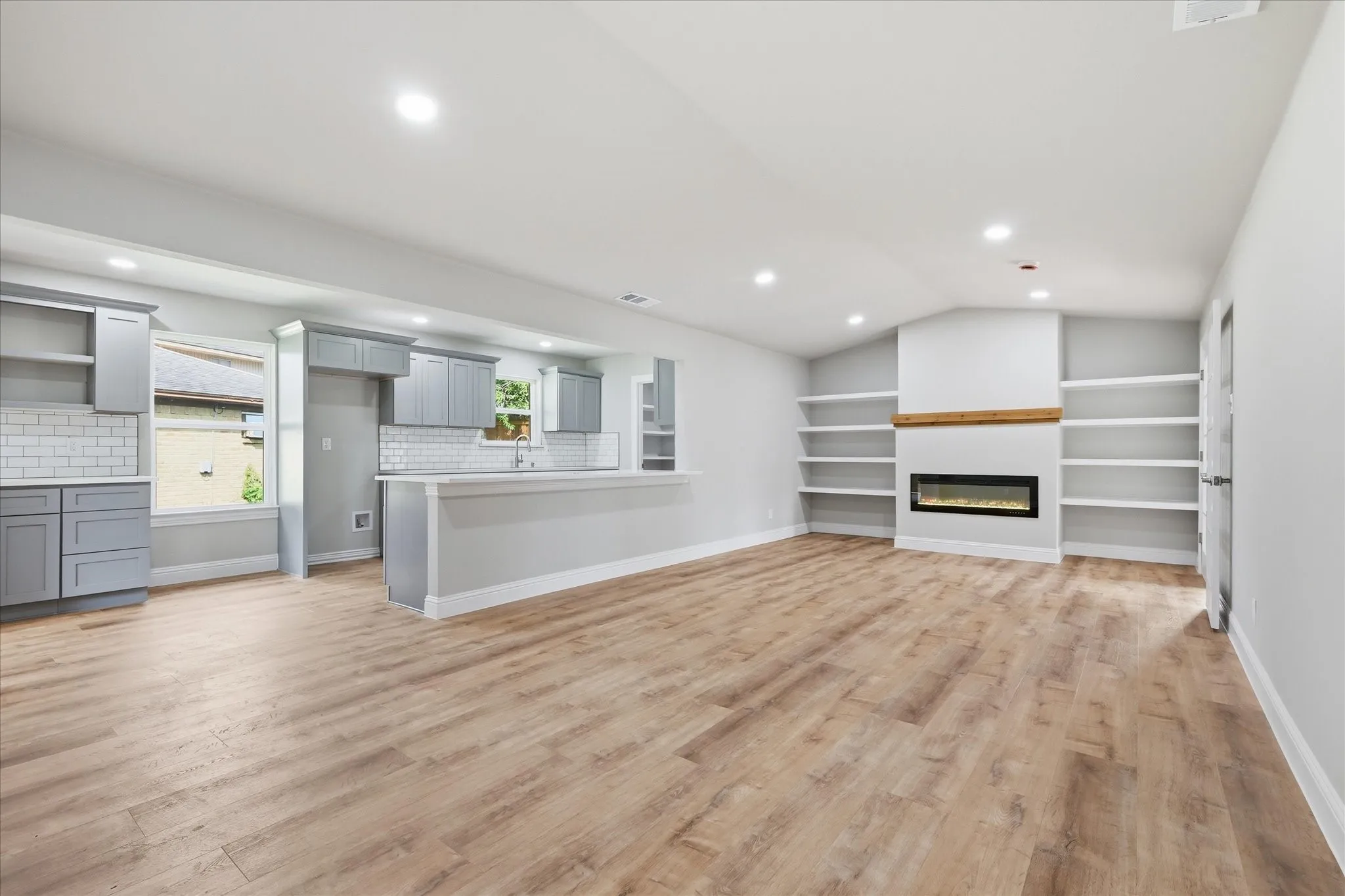 Open-concept living area with wood-finish flooring, recessed lighting, and a linear electric fireplace