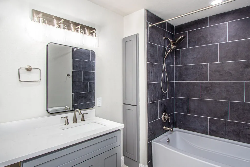 Contemporary bathroom featuring a vanity with integrated sink, brushed nickel fixtures, a rectangular mirror, and a wall-mounted light bar