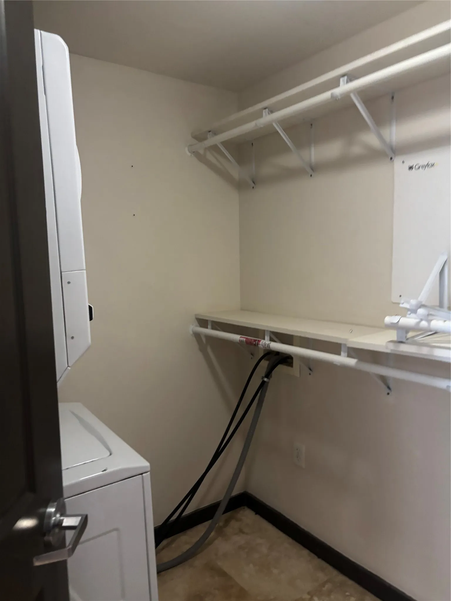 Dedicated laundry area featuring a stacked washer and dryer unit, wire shelving, and a built-in shelf