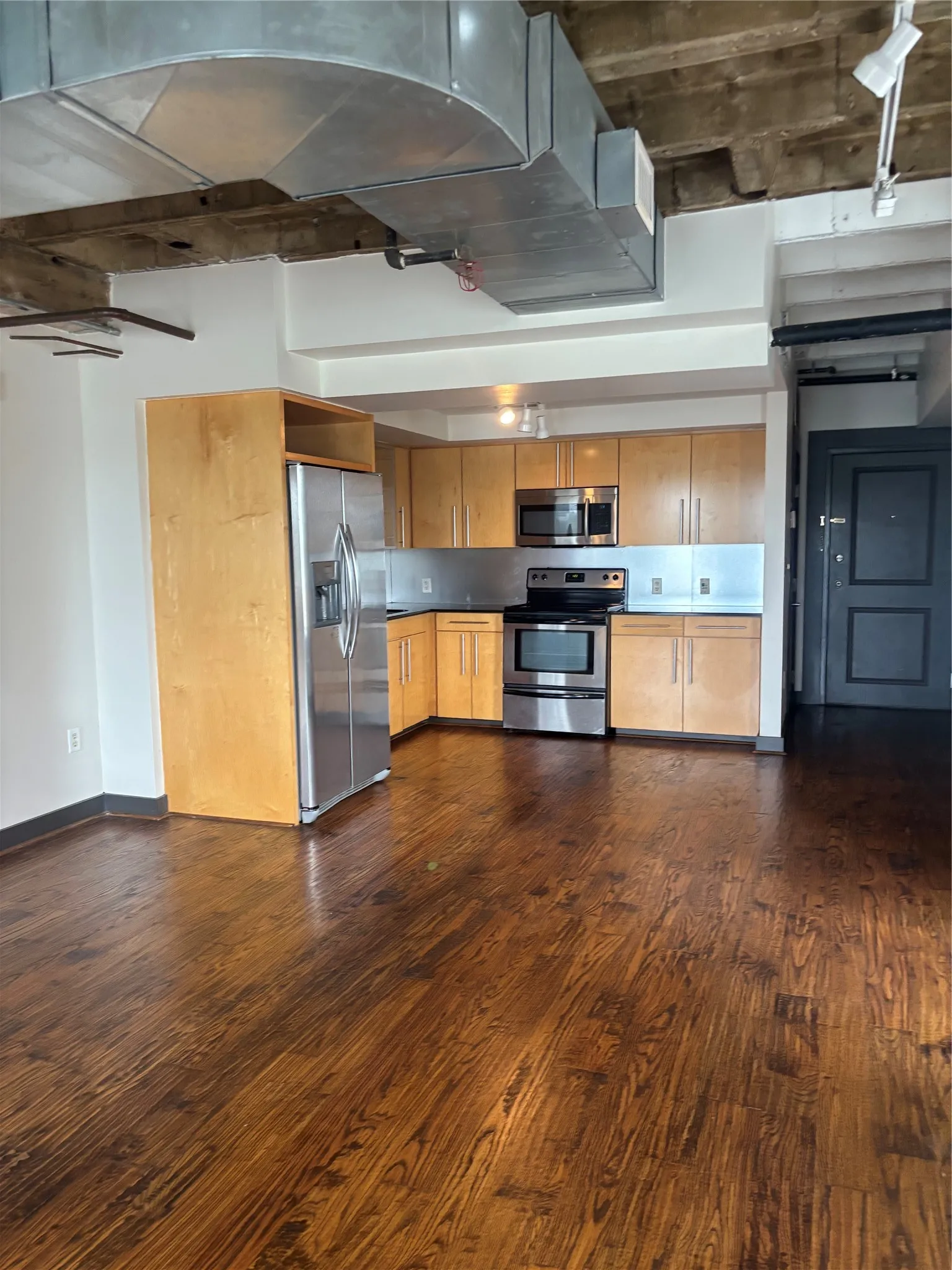 Open-concept kitchen with wood-finish flooring, stainless steel appliances, and light wood cabinetry