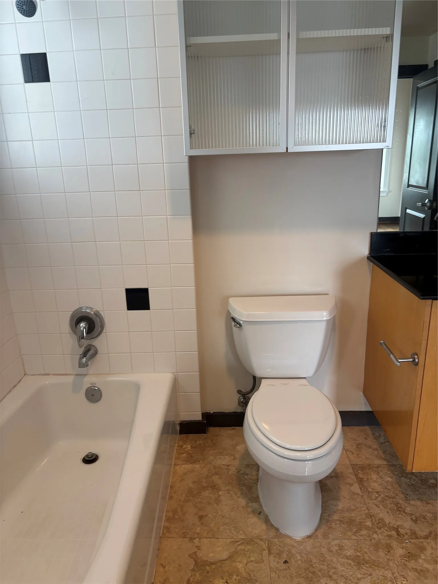 Bathroom featuring a white tub, white wall tiling with black accent tiles, and a white toilet
