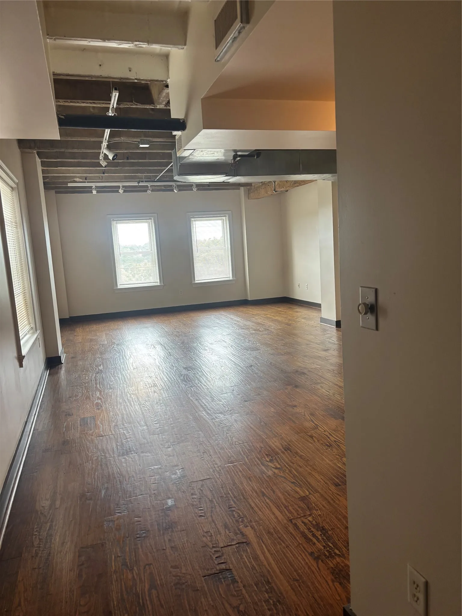 Spacious interior featuring wood-finish flooring, multiple windows, exposed ceiling infrastructure, and track lighting