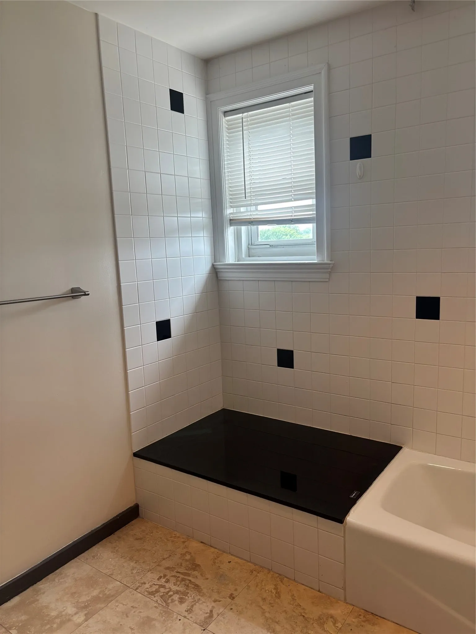 White tiled bathroom with contrasting black accent tiles, featuring a built-in bench with a dark countertop