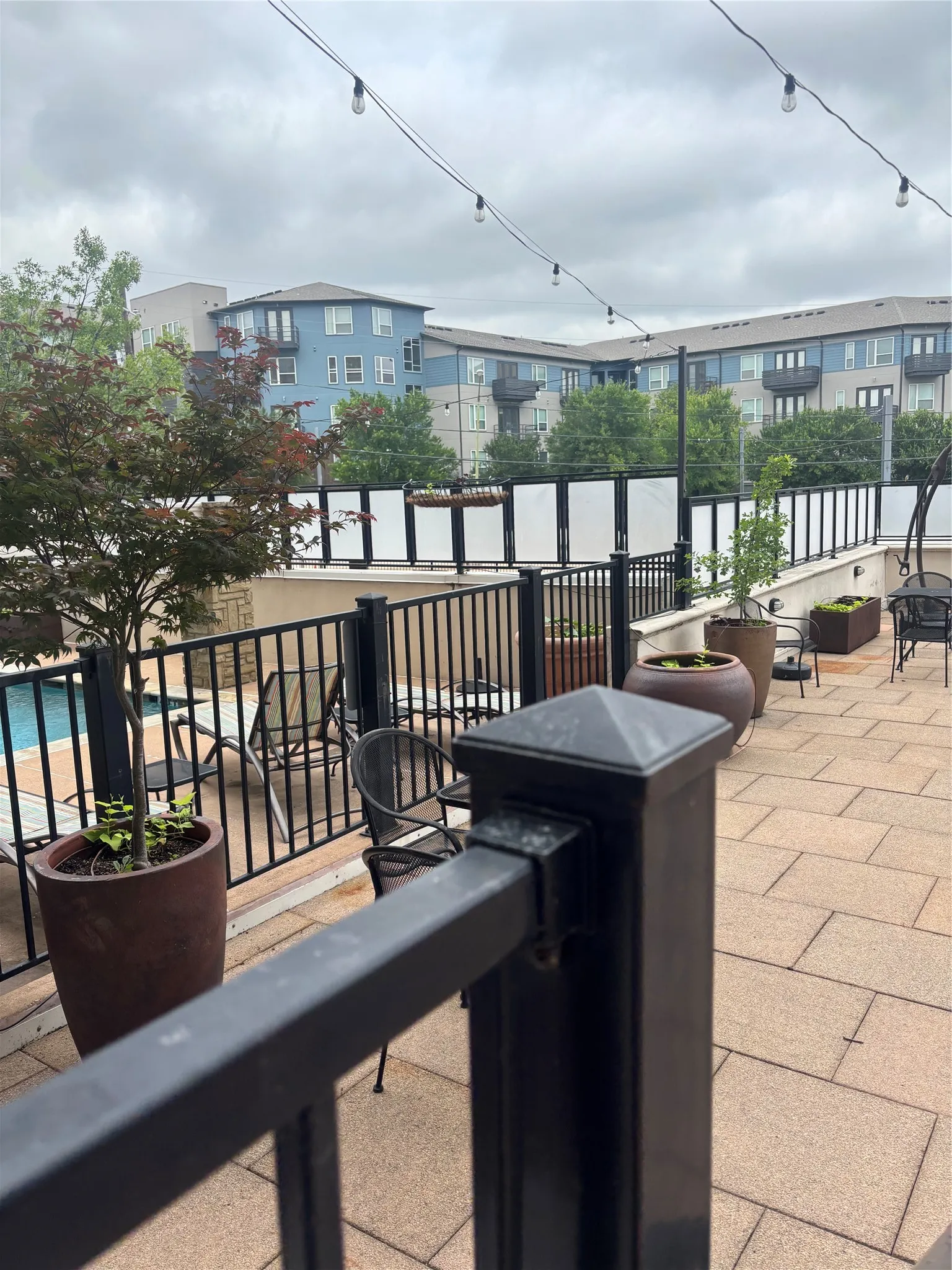 Paved patio area featuring string lighting, black metal railings, and container plantings