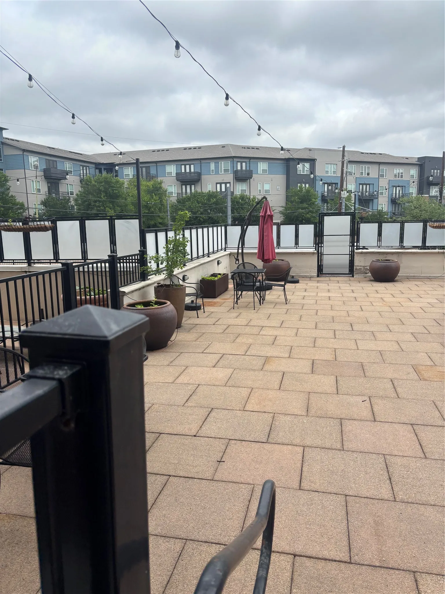 Expansive paved patio space featuring string lighting, privacy screens, and dark metal railings