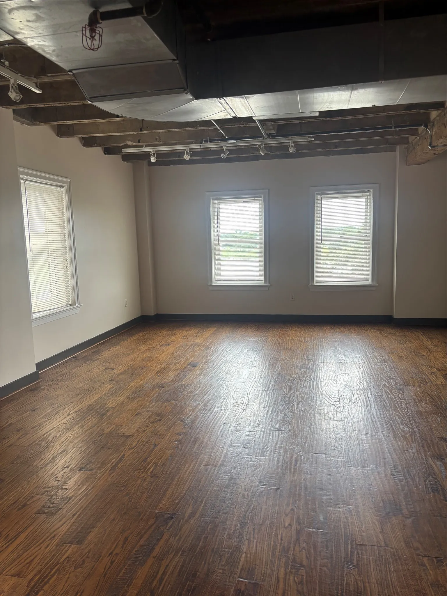 Spacious room featuring wood-finish flooring, exposed ceiling beams, and industrial-style ductwork