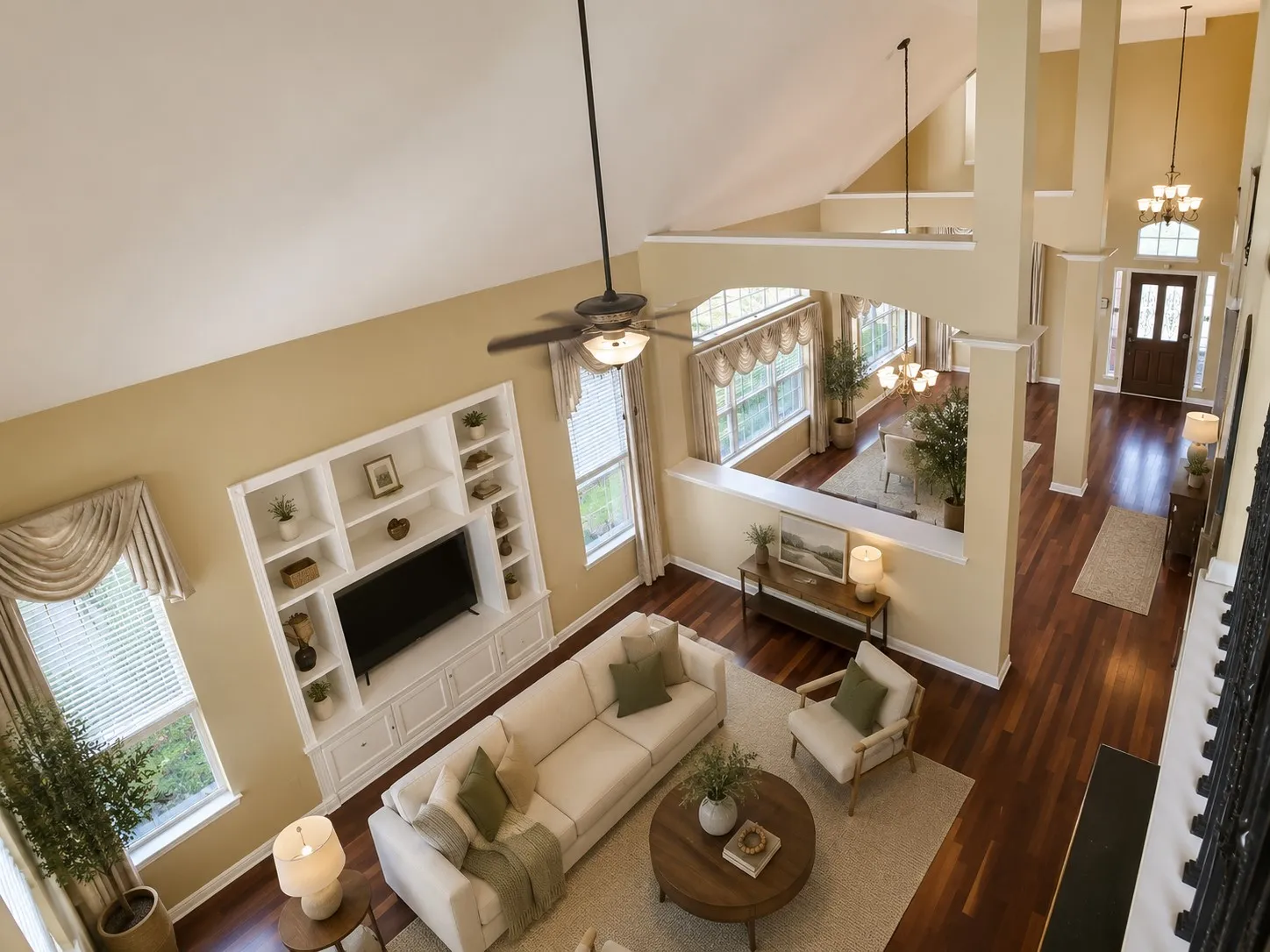 Two-story living area featuring a vaulted ceiling with a ceiling fan, a built-in media center with shelving, and wood-finish flooring