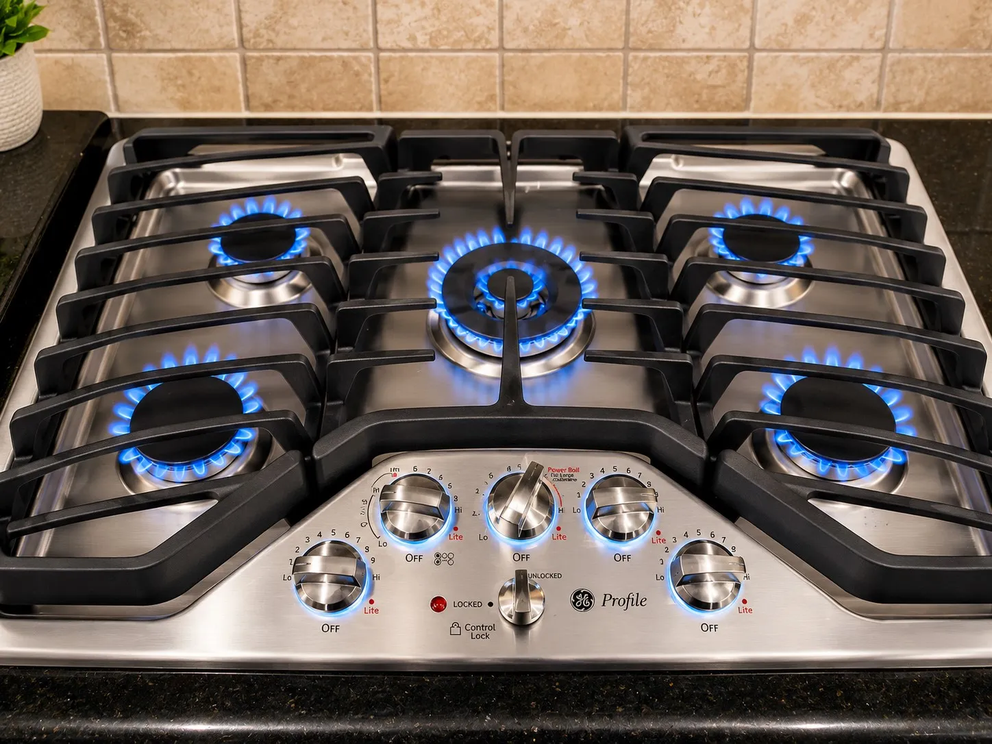 Stainless steel gas cooktop with five burners and continuous grates, set into a dark countertop