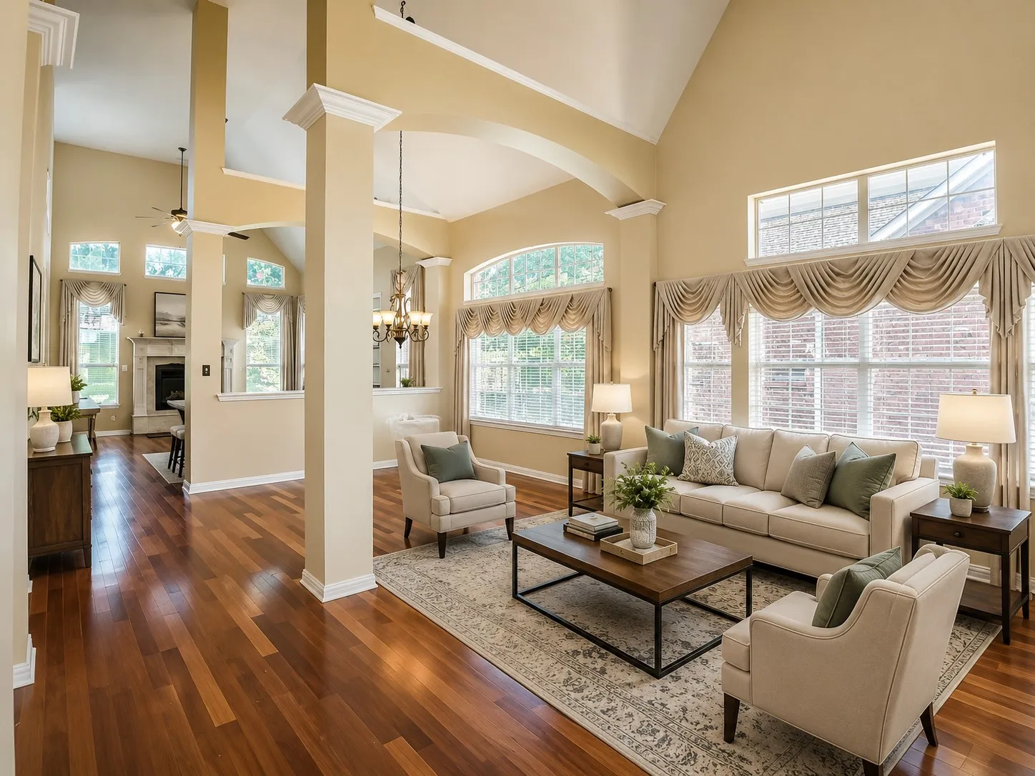 Spacious living area featuring high vaulted ceilings, expansive windows, wood-finish flooring, architectural columns, and a fireplace with a mantel