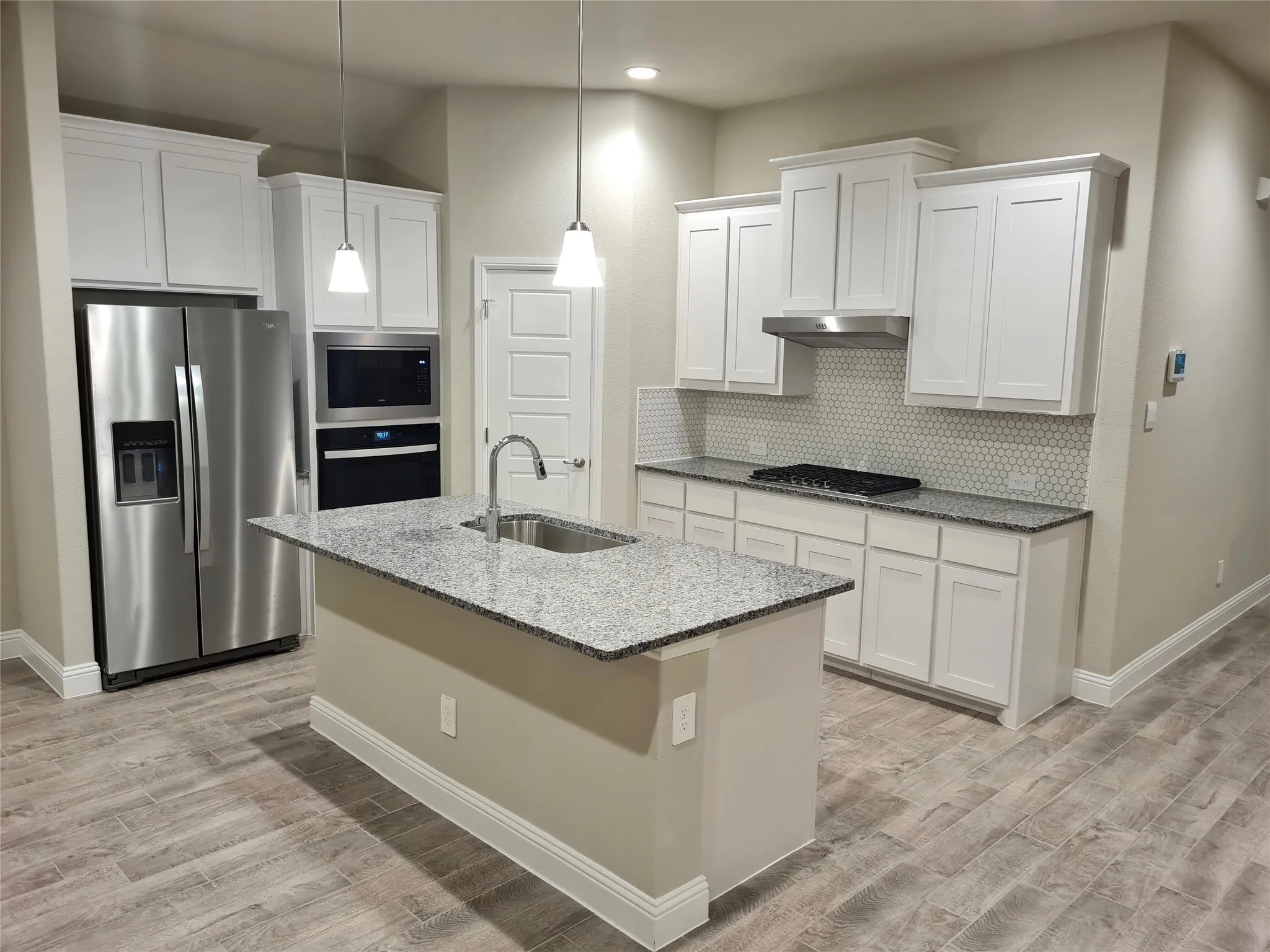 Kitchen with tasteful backsplash, decorative Pendant lights, sink, white cabinets and appliances with stainless steel finishes.