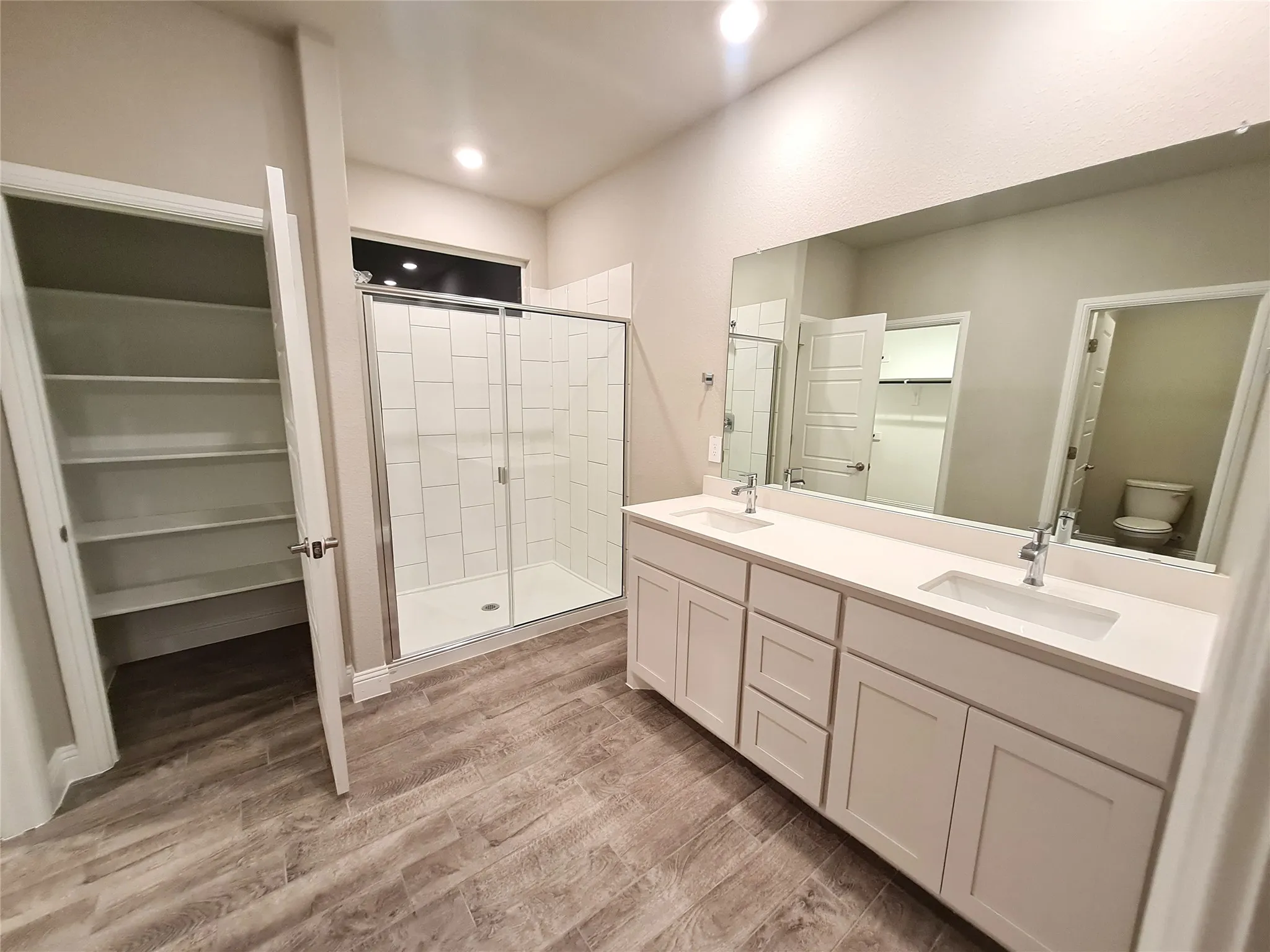 Master Bath with wood-type ceramic flooring, vanity with extensive cabinet space, large separate shower, toilet, dual vanity sinks, and linen closet.