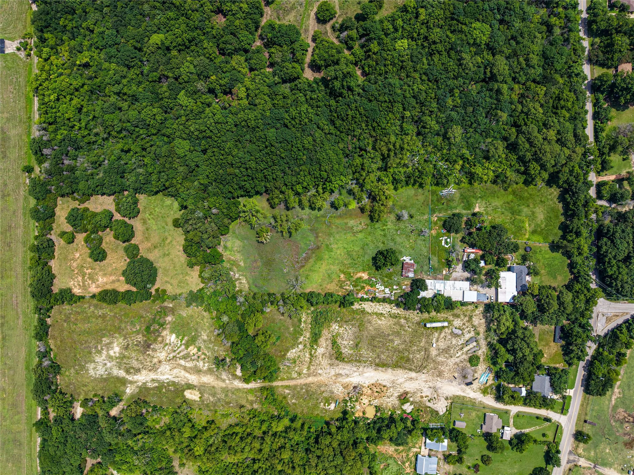 Expansive land parcel featuring dense tree coverage, multiple clearings, and existing structures
