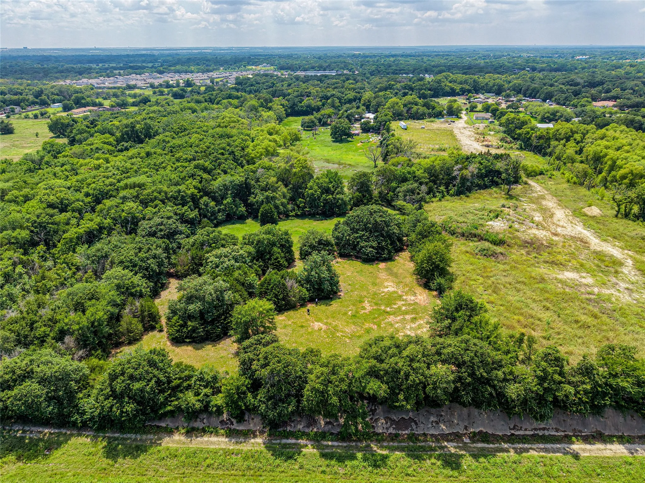 Expansive aerial view of a verdant landscape featuring mature trees, open grassy areas, and distant residential structures