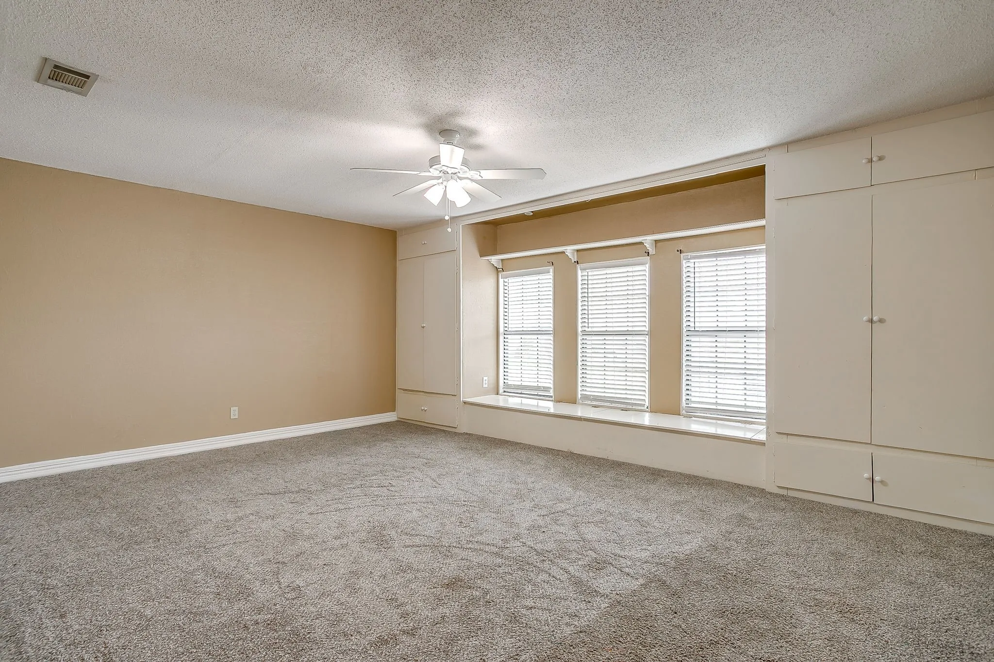 Expansive room featuring plush gray carpeting, neutral wall tones, and a ceiling fan