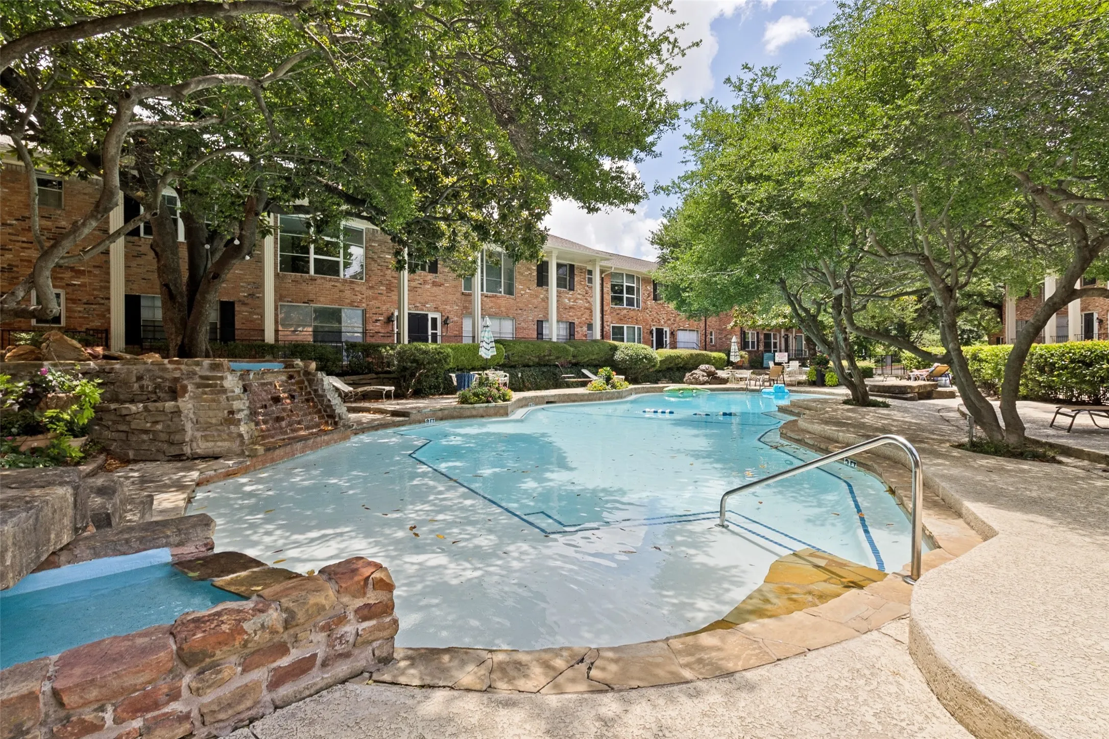 Swimming pool with integrated stone-clad water features and a surrounding concrete patio