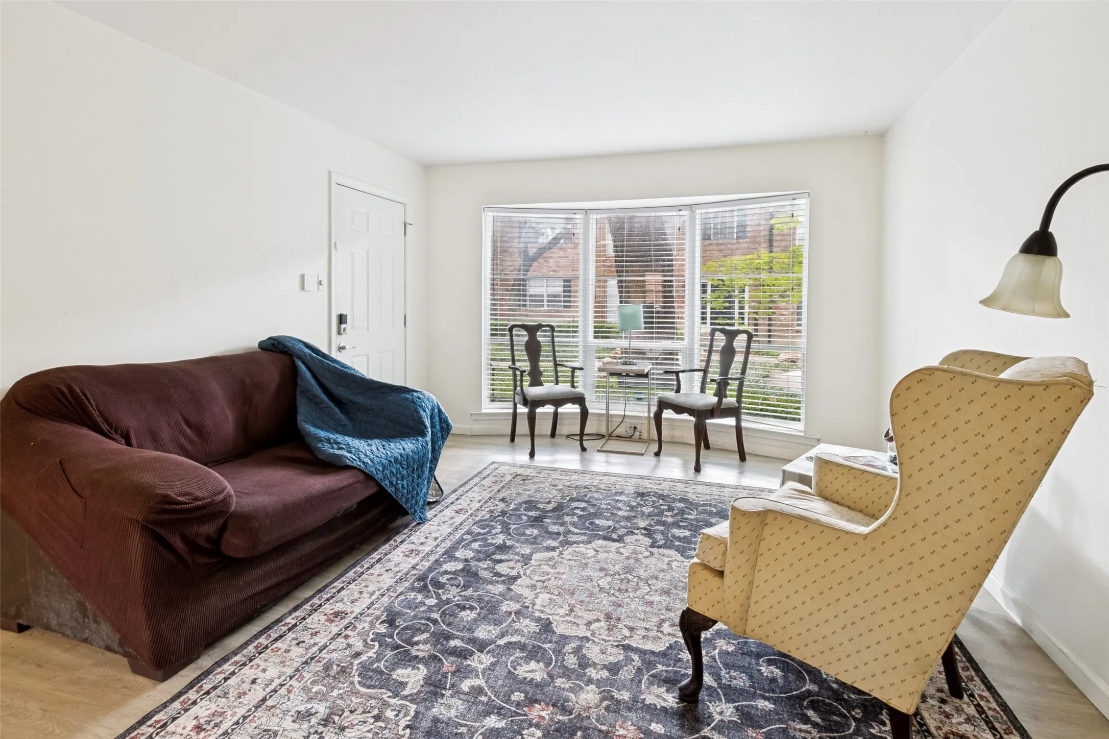 Bright living area featuring a bay window with blinds, light wall tones, a paneled entry door, and light-toned flooring