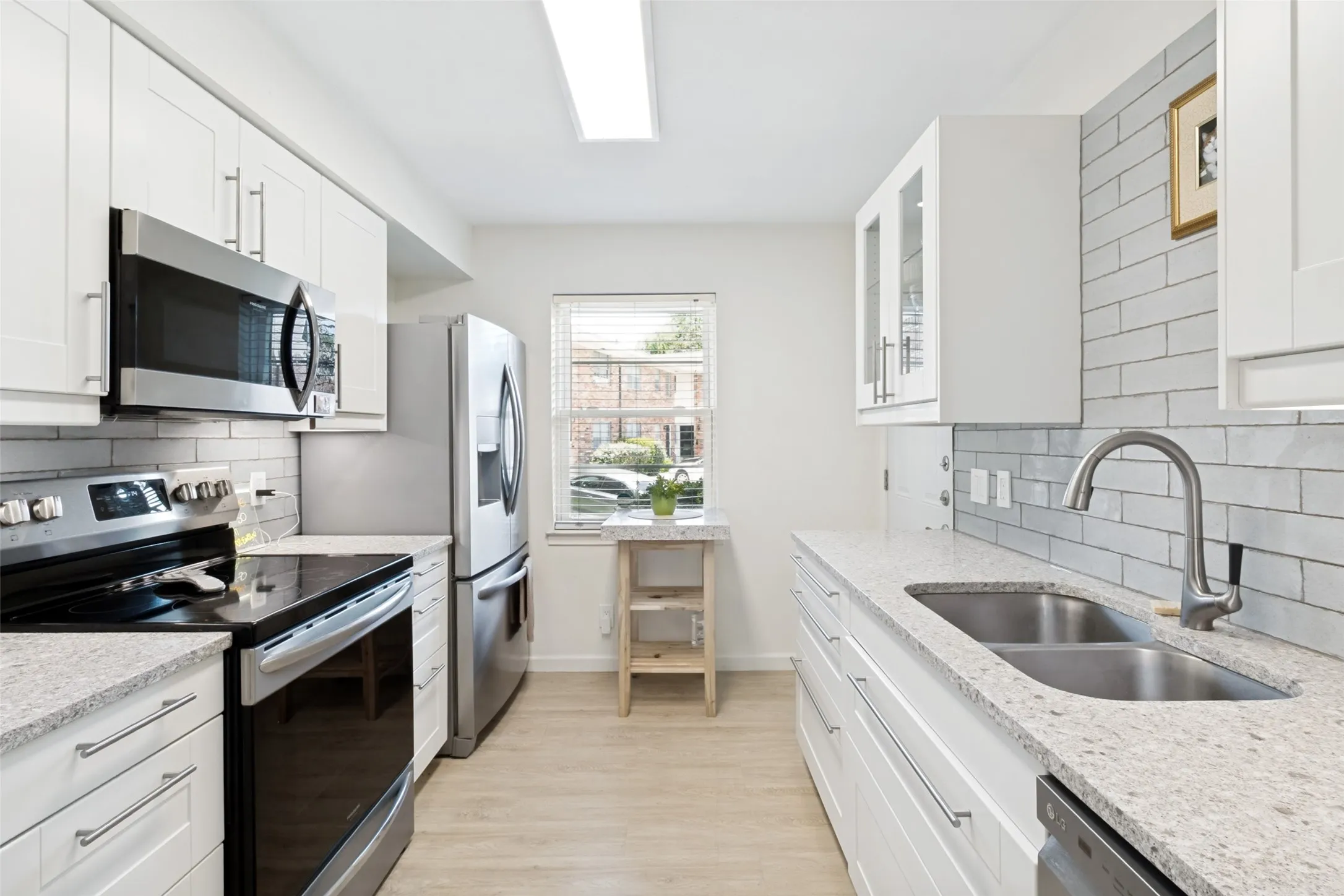 Galley kitchen featuring white shaker cabinetry, stainless steel appliances, light-toned countertops, a subway tile backsplash, and wood-finish flooring