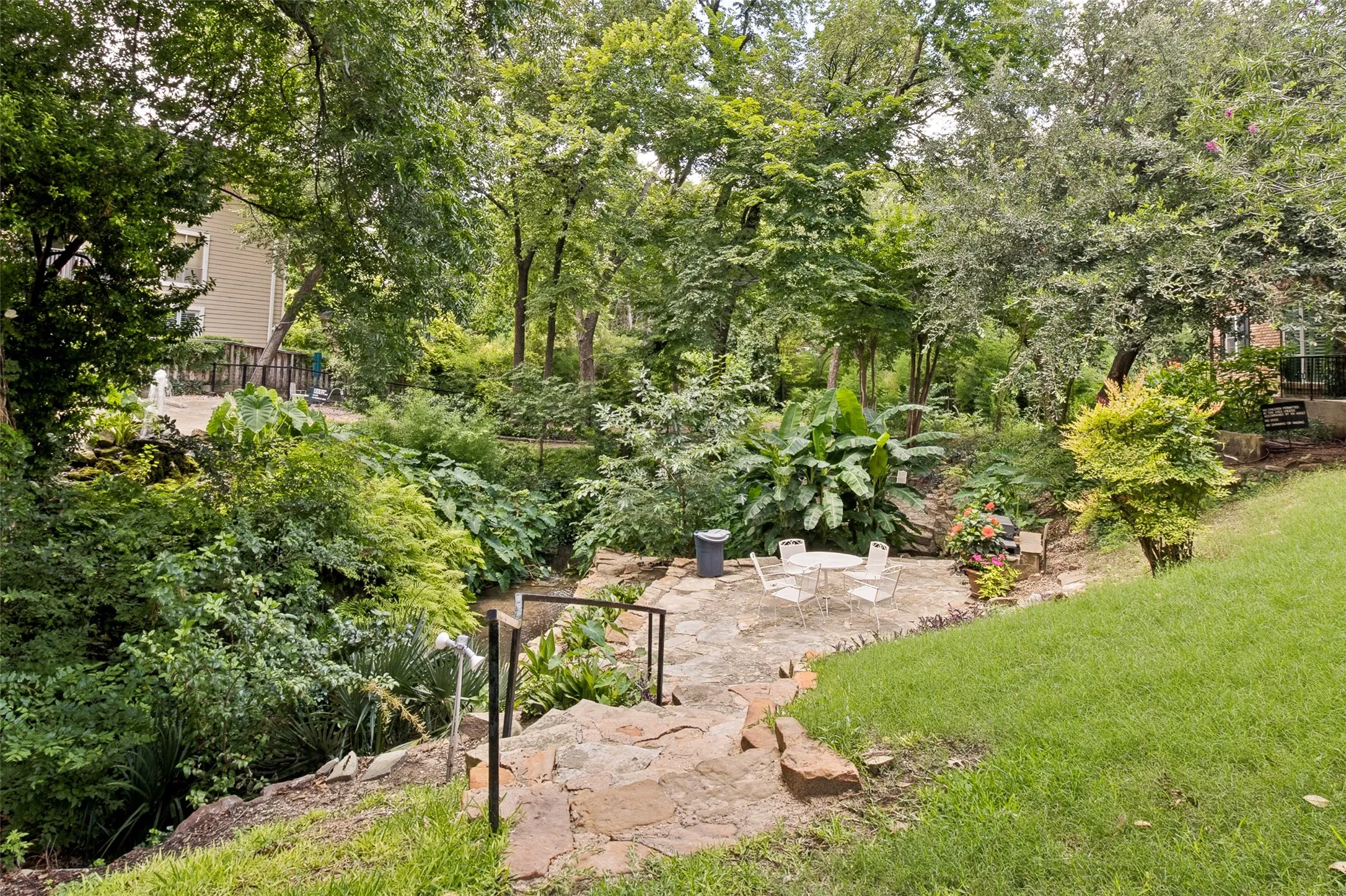 Tiered backyard featuring a stone patio, mature trees, and lush landscaping