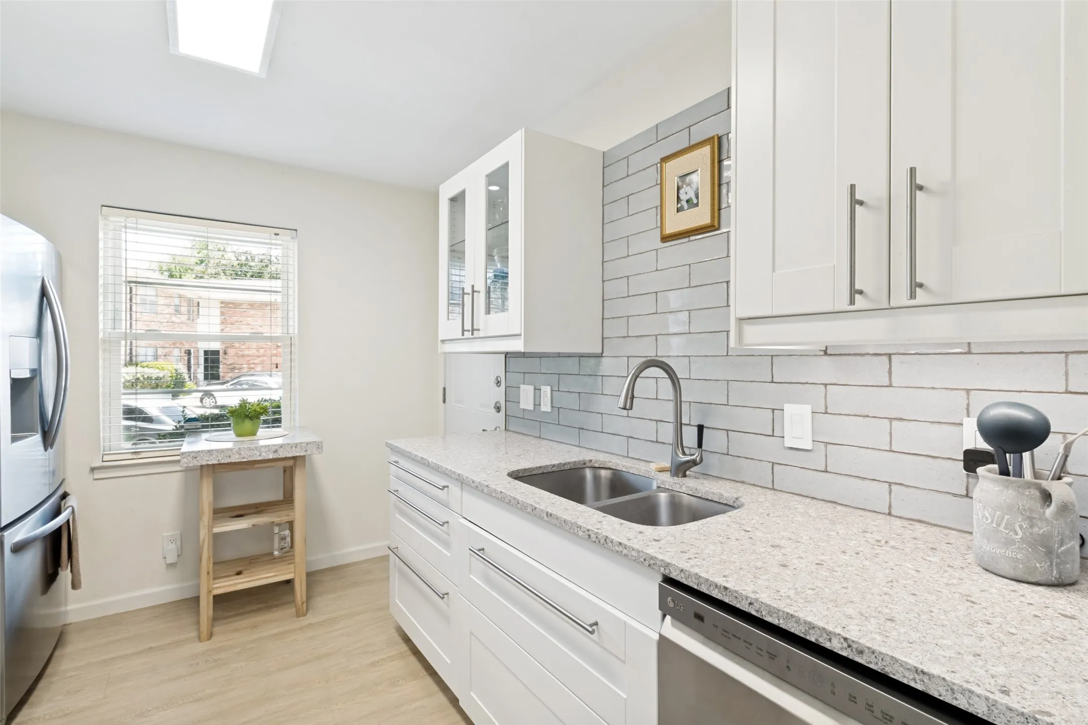 Kitchen featuring white shaker-style cabinetry, light speckled countertops, a stainless steel double basin sink with a gooseneck faucet, and a light gray subway tile backsplash