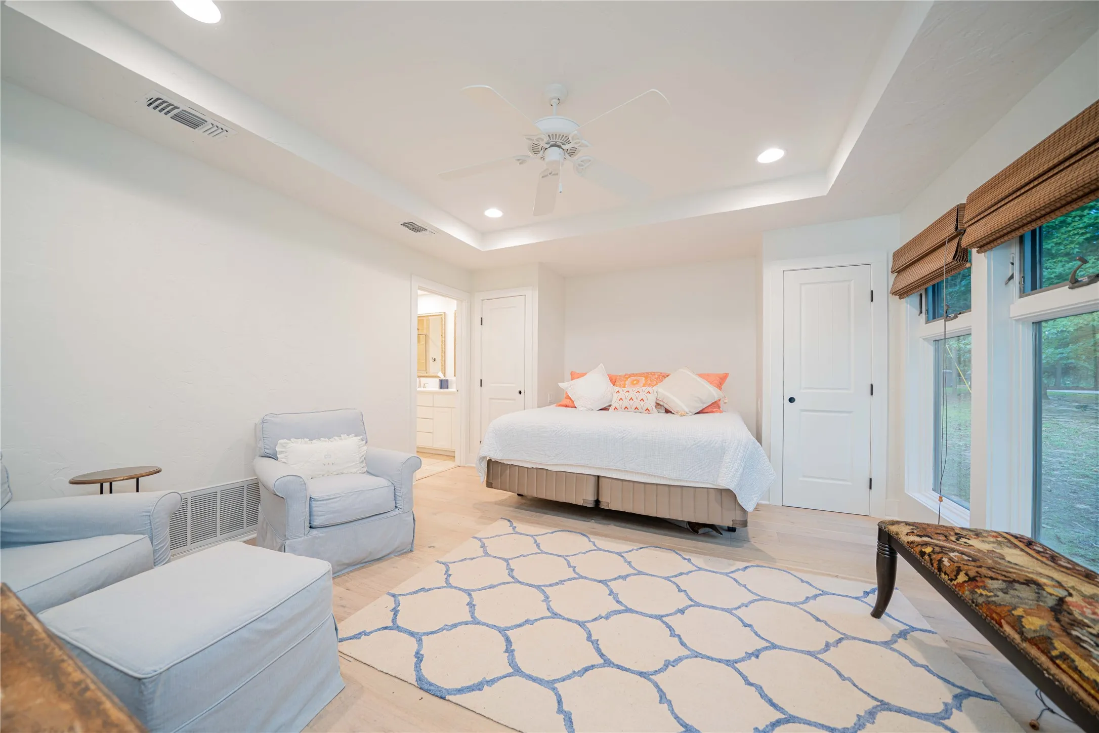Bedroom with recessed lighting, a raised ceiling, light wood-style flooring, ceiling fan, and connected bathroom