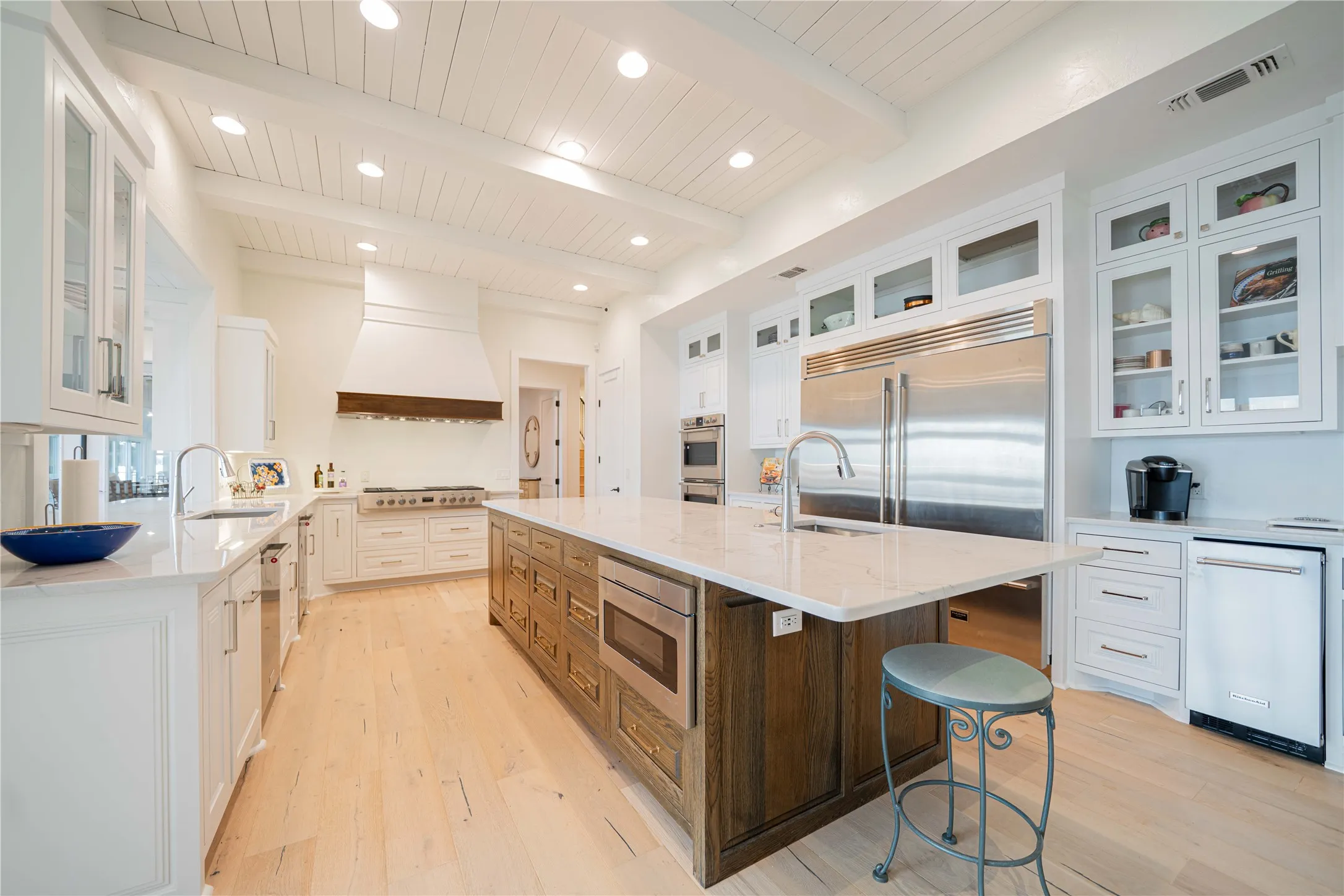 Kitchen with built in appliances, custom exhaust hood, light wood-style floors, a large island, and a kitchen bar