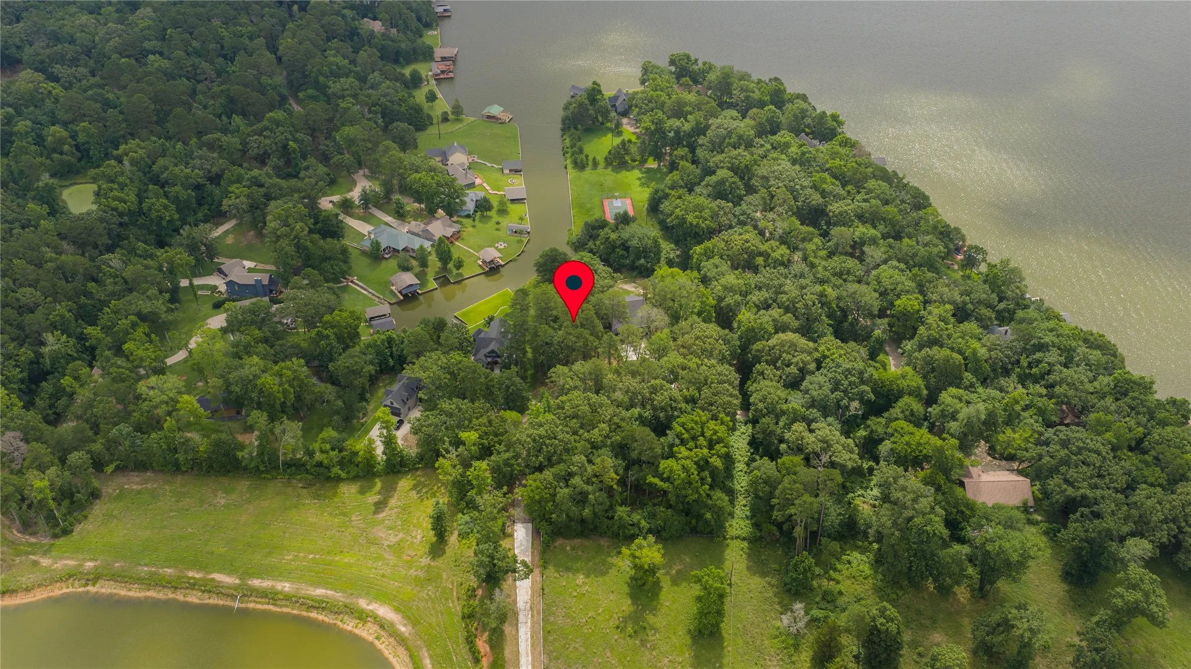 Aerial perspective showcasing a wooded peninsula with waterfront properties and a visible red marker indicating a specific property