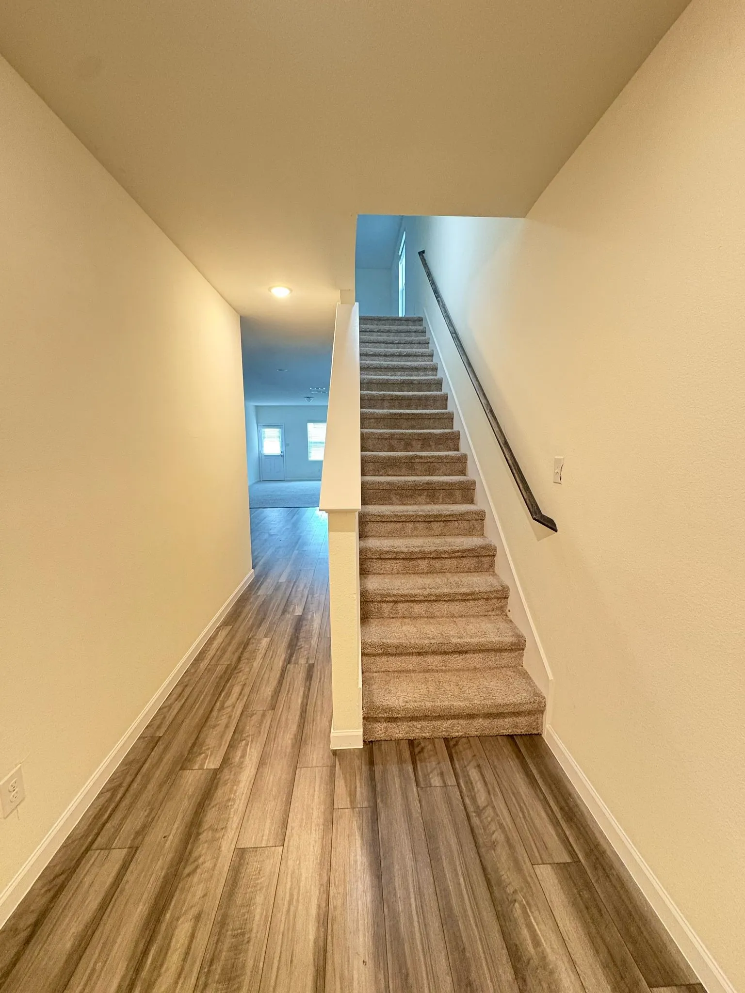 Staircase with carpeted treads and risers, featuring a dark handrail and white newel post