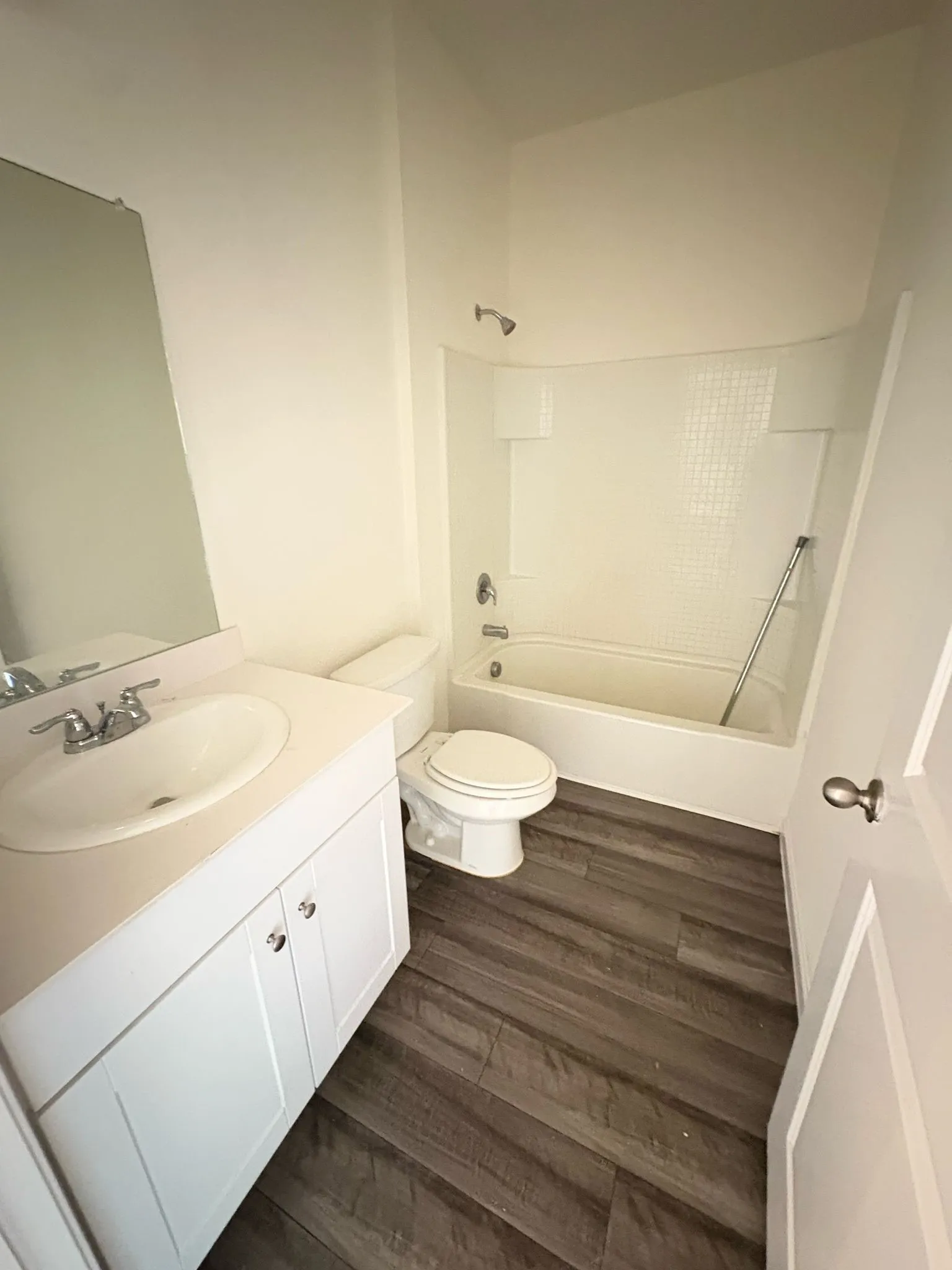 Full bathroom featuring a white vanity with integrated sink, wood-finish flooring, a toilet, and a bathtub with a shower