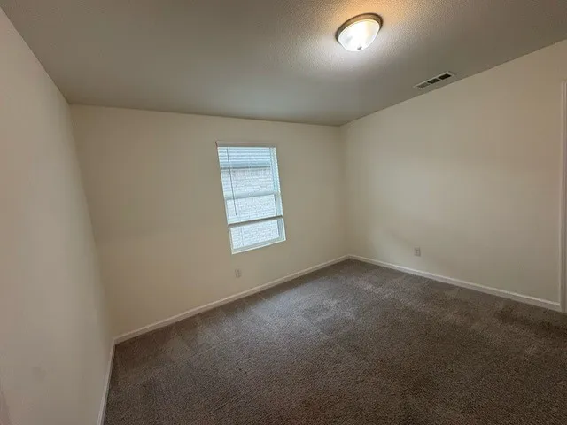 Carpeted room featuring a window with blinds, a ceiling-mounted light fixture, and a ceiling vent