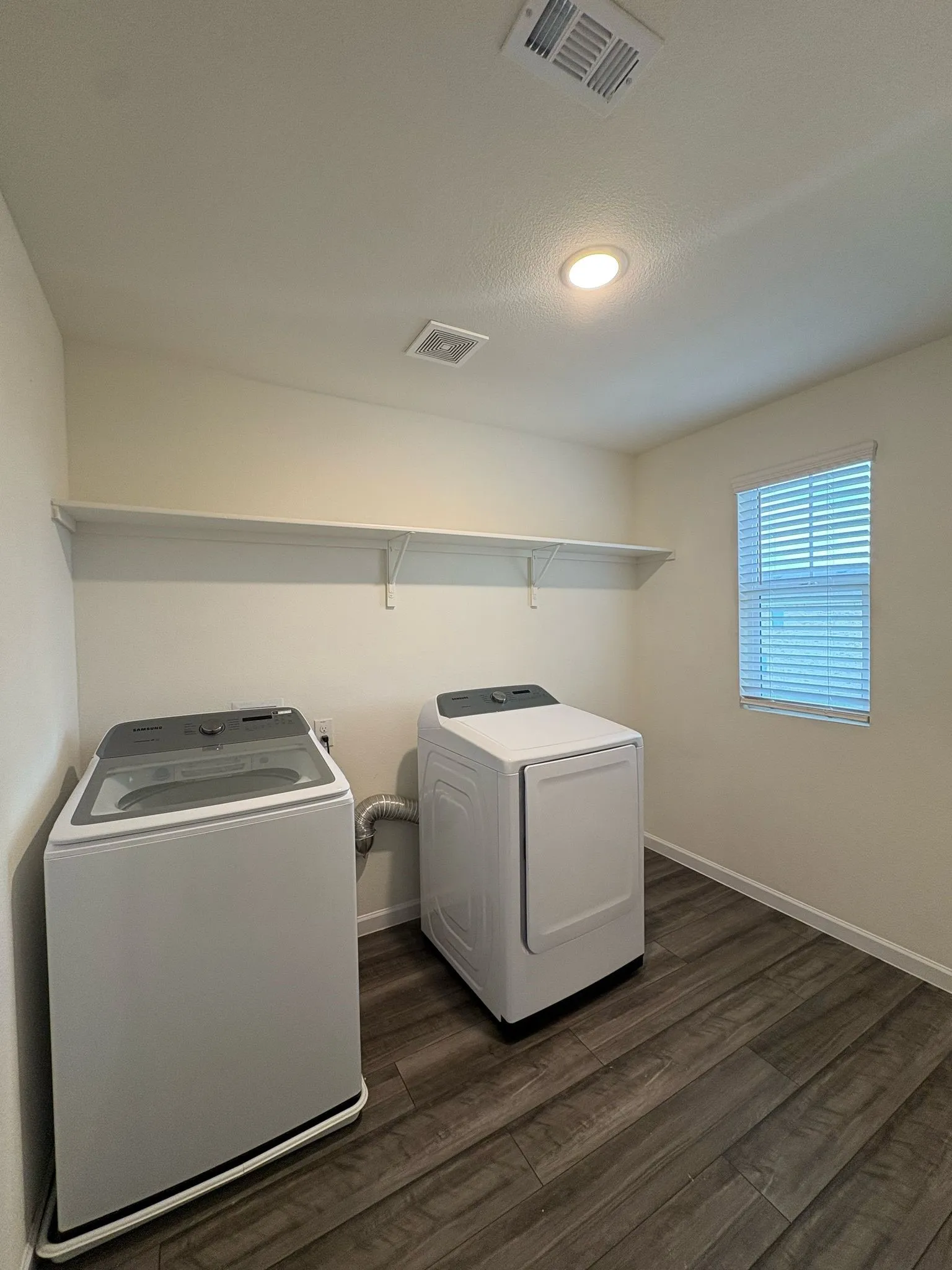 Dedicated laundry area featuring durable wood-finish flooring, recessed lighting, and a window with blinds