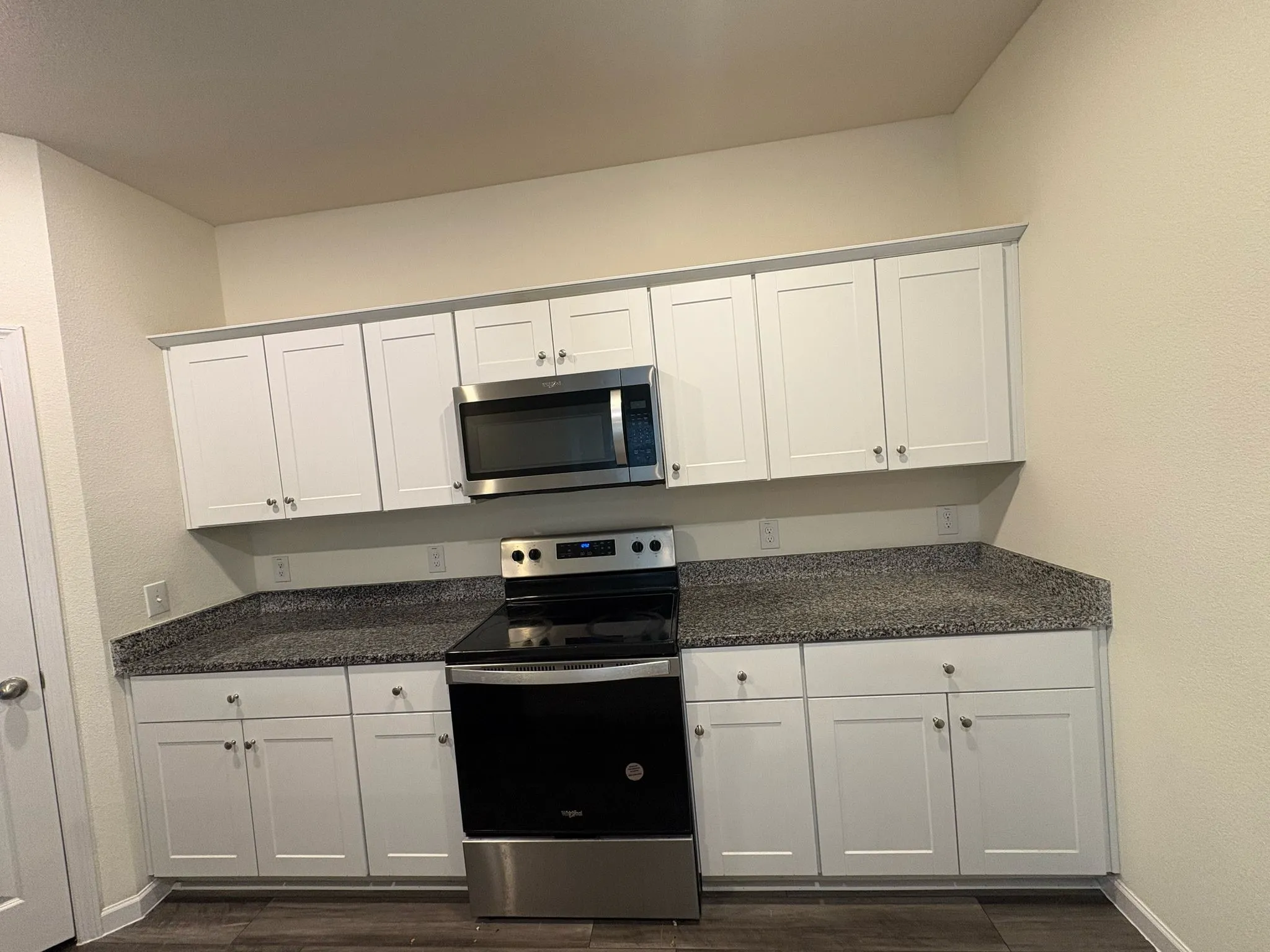Kitchen featuring white shaker cabinetry, stainless steel range, built-in stainless steel microwave, speckled countertops, and wood-finish flooring