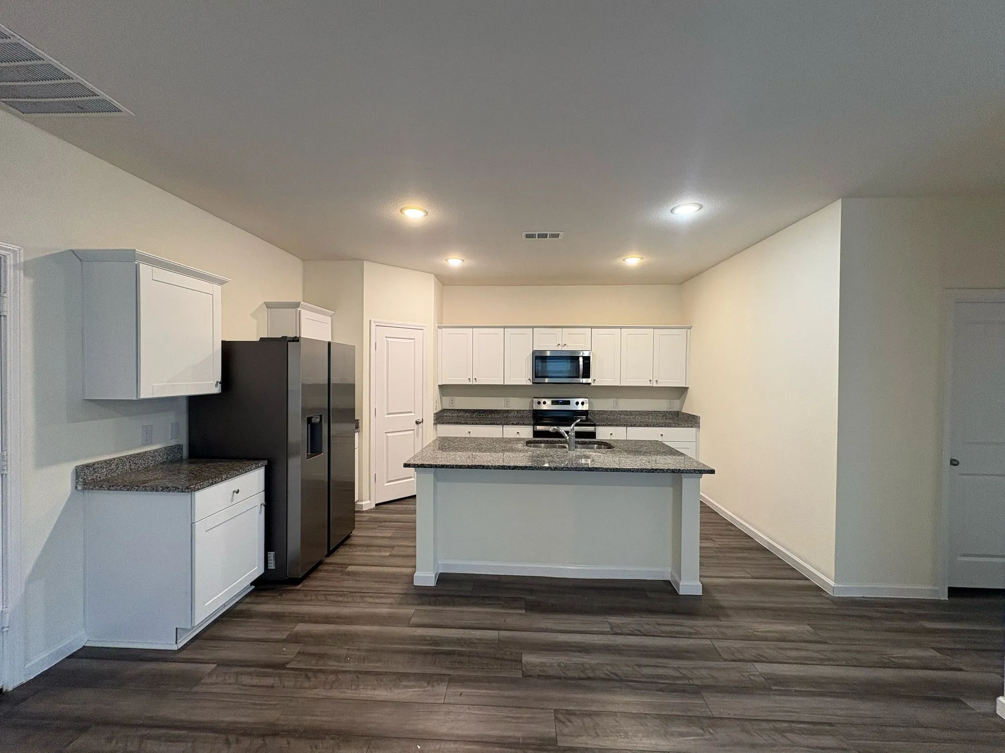 Contemporary kitchen featuring white cabinetry, dark wood-finish flooring, a central island with an undermount sink, recessed lighting, and granite-style countertops
