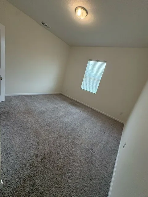 Interior room featuring sloped ceilings, a single window with horizontal blinds, and wall-to-wall carpeting