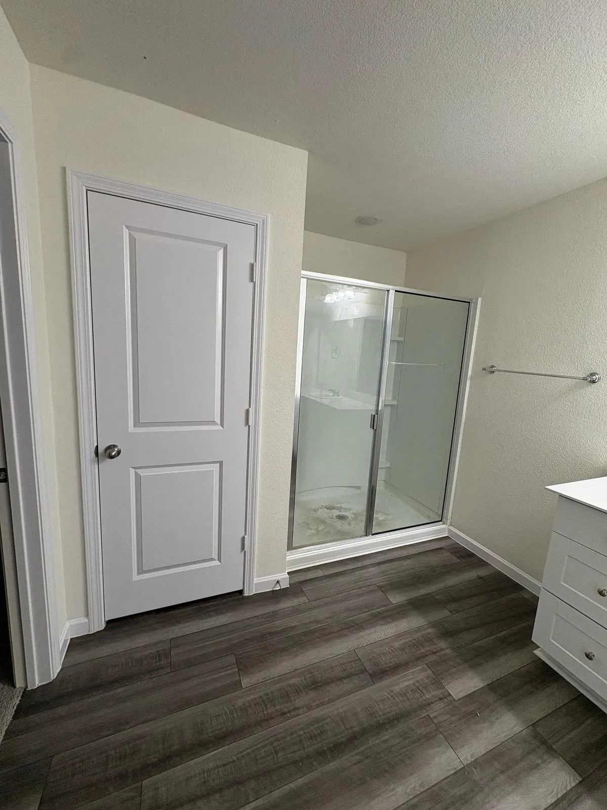 Bathroom featuring dark wood-finish flooring, a glass-enclosed shower, a white vanity with drawers, a wall-mounted towel bar, and a two-panel interior door