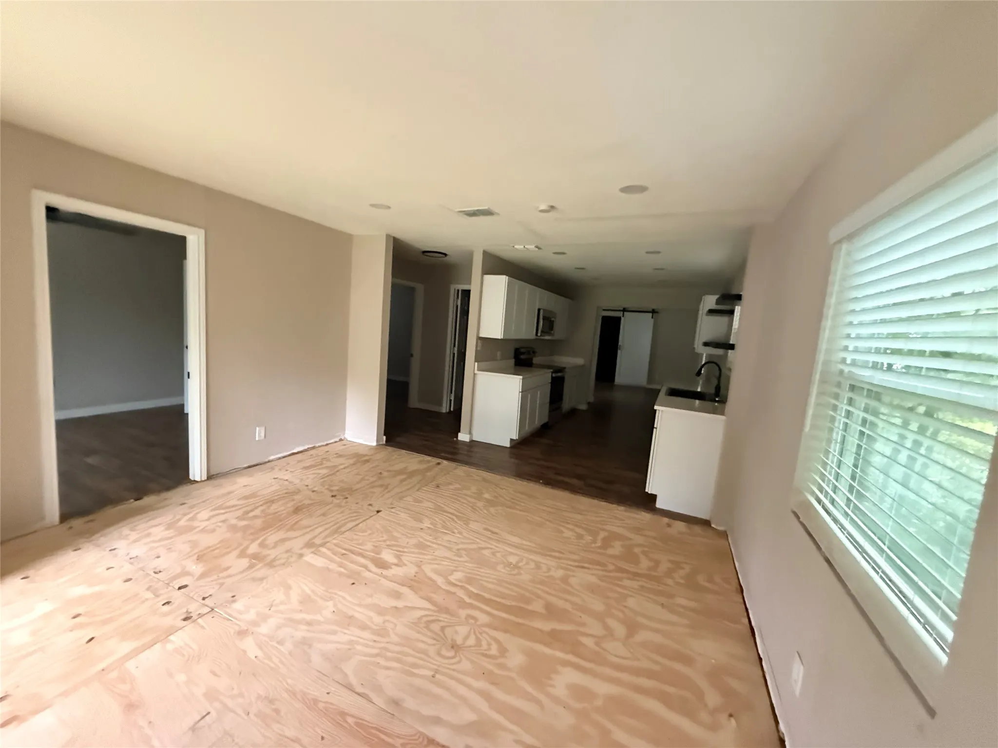 Open-concept living space featuring a partial plywood subfloor, light neutral wall paint, and white trim