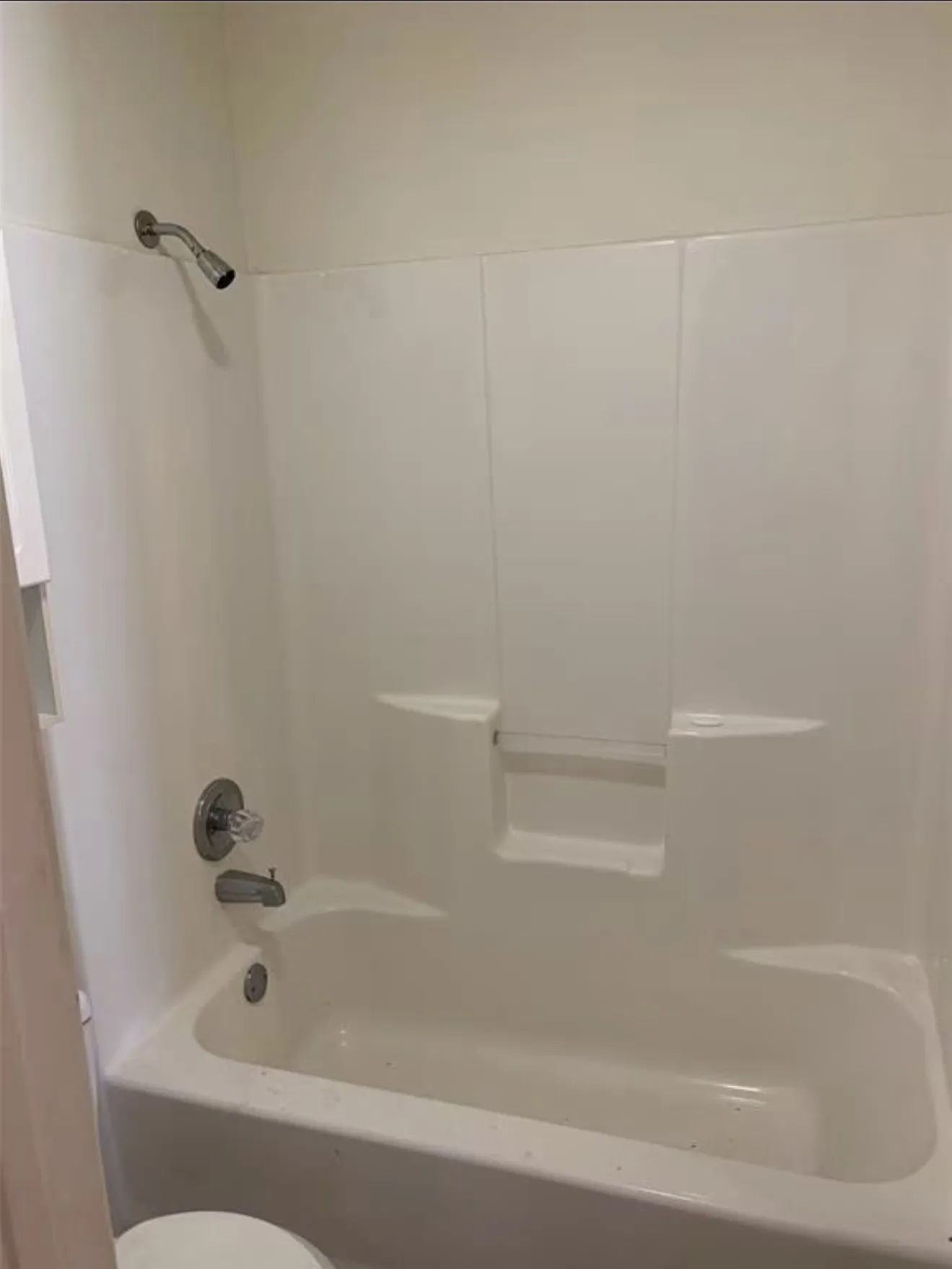 White bathtub with an integrated shower surround, stainless steel showerhead, and coordinating bath faucet