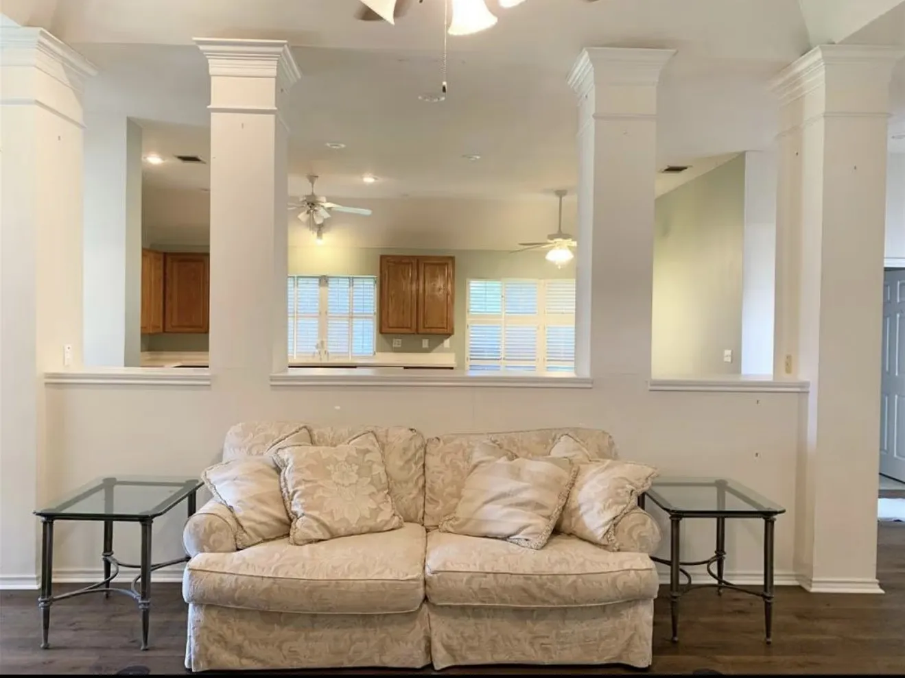 Living area featuring decorative columns with crown molding, wood-finish flooring, and a half-wall opening to the kitchen