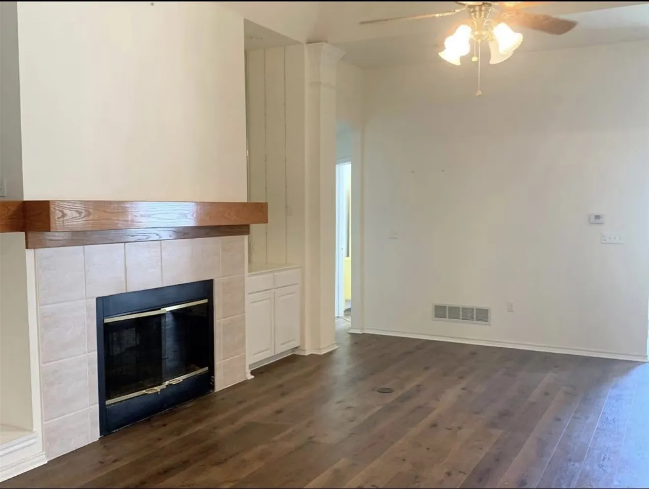 Living area featuring a tiled fireplace with a wood mantle, built-in cabinetry, wood-finish flooring, and a ceiling fan with integrated lighting