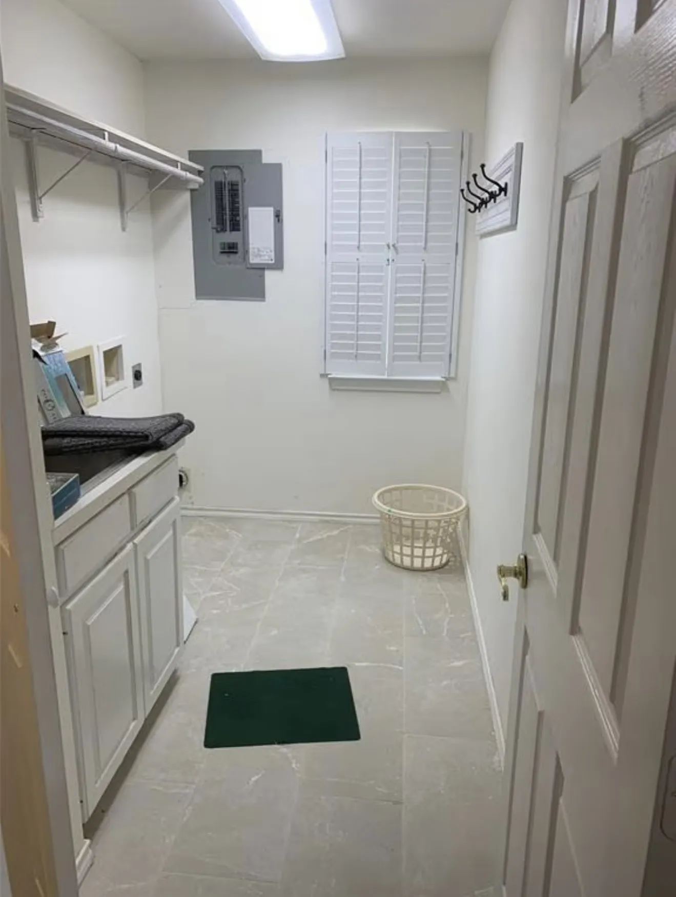 Utility room featuring a white paneled door, built-in shelving, white plantation shutters, and light-toned tile flooring